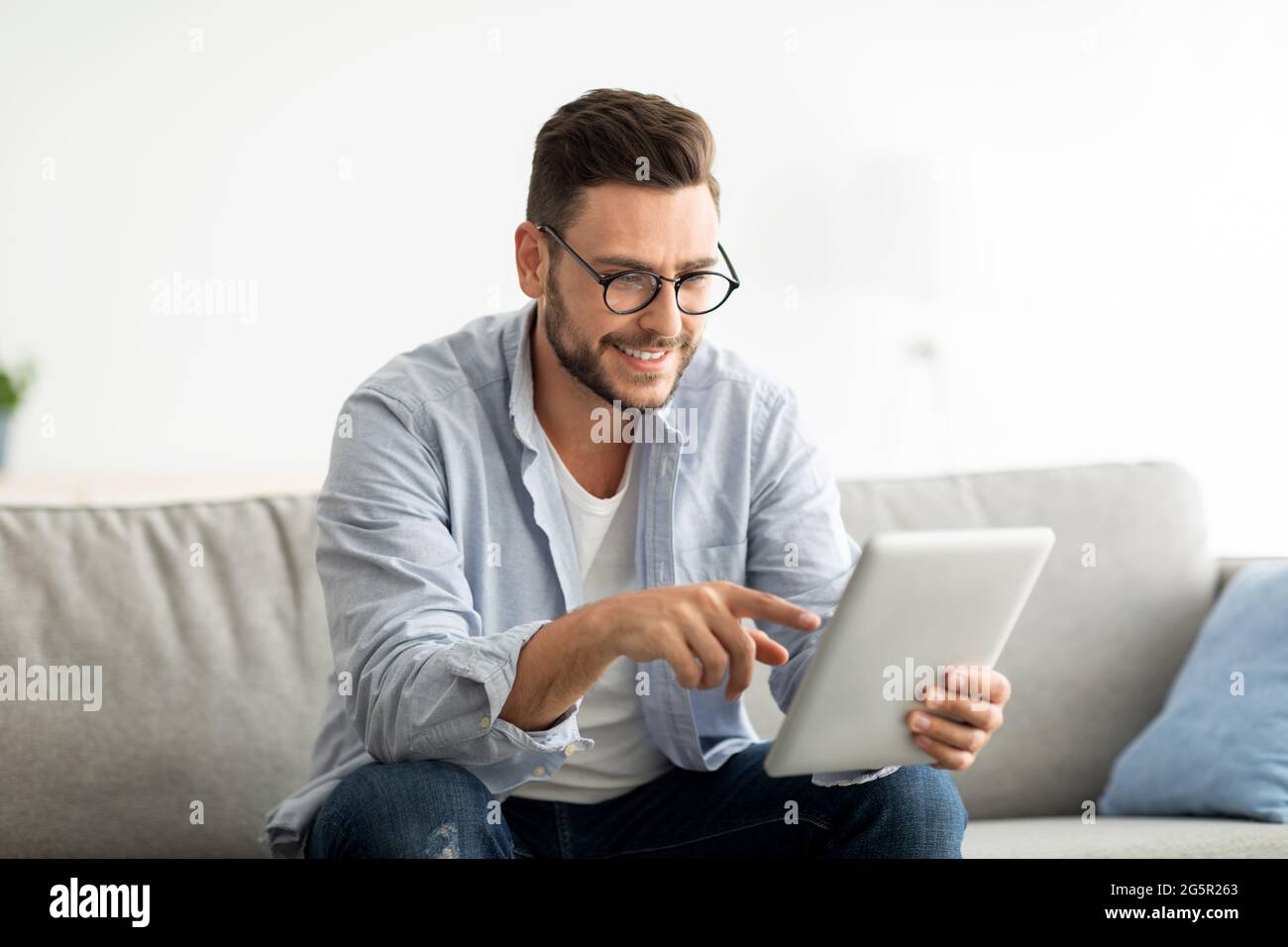 Concetto di tempo libero. Uomo felice che usa un tablet digitale, seduto sul divano in soggiorno, spazio per la copia Foto Stock