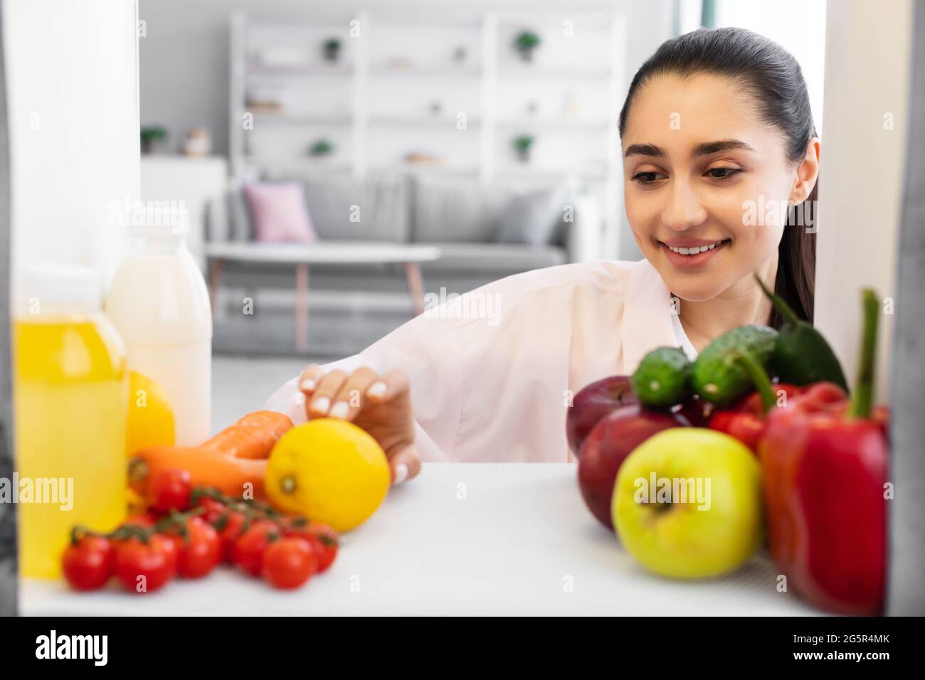 Donna sorridente che apre il frigorifero e prende il cibo Foto Stock