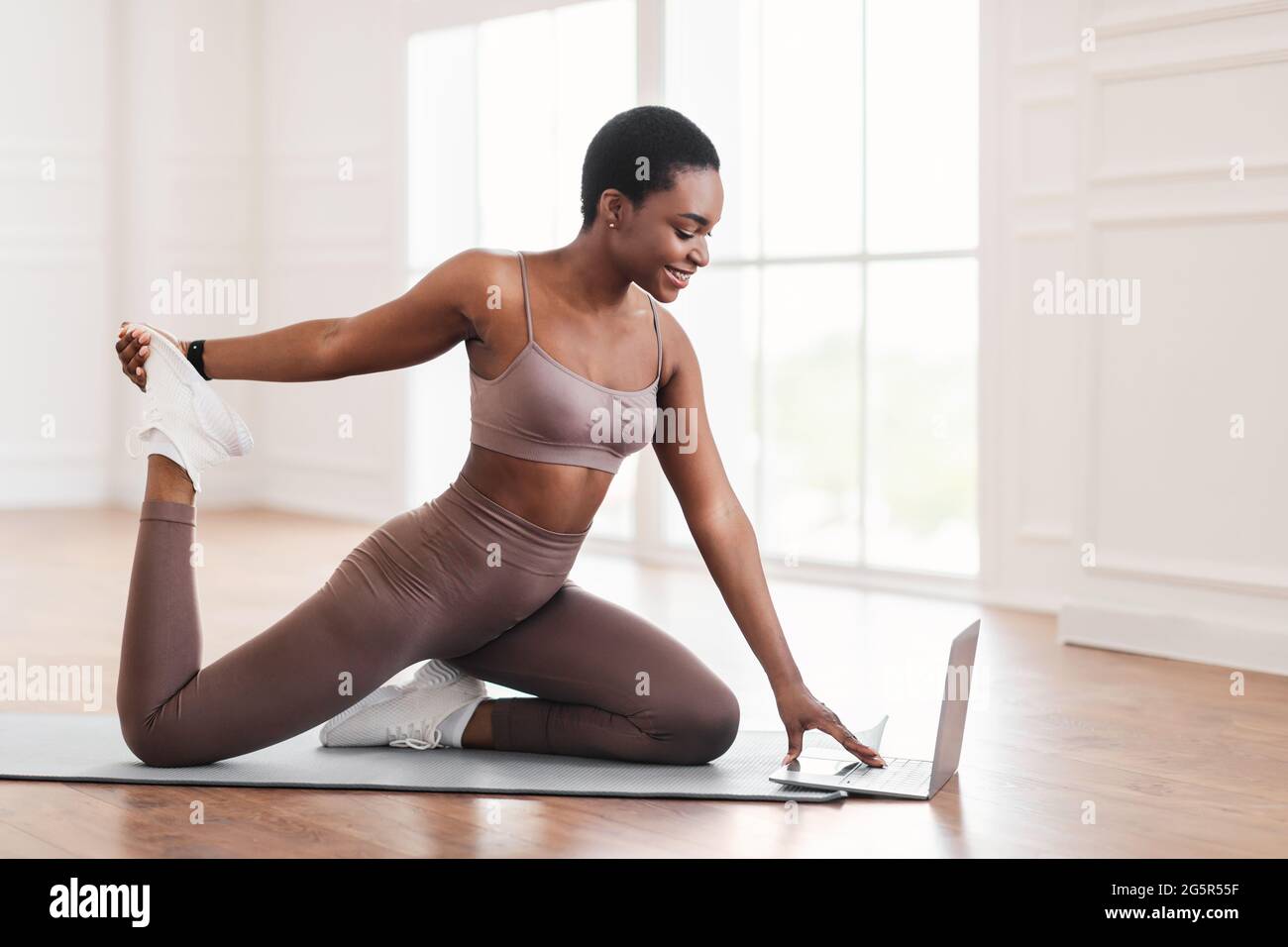 Allegra donna nera che allunga i muscoli delle gambe usando un computer portatile Foto Stock