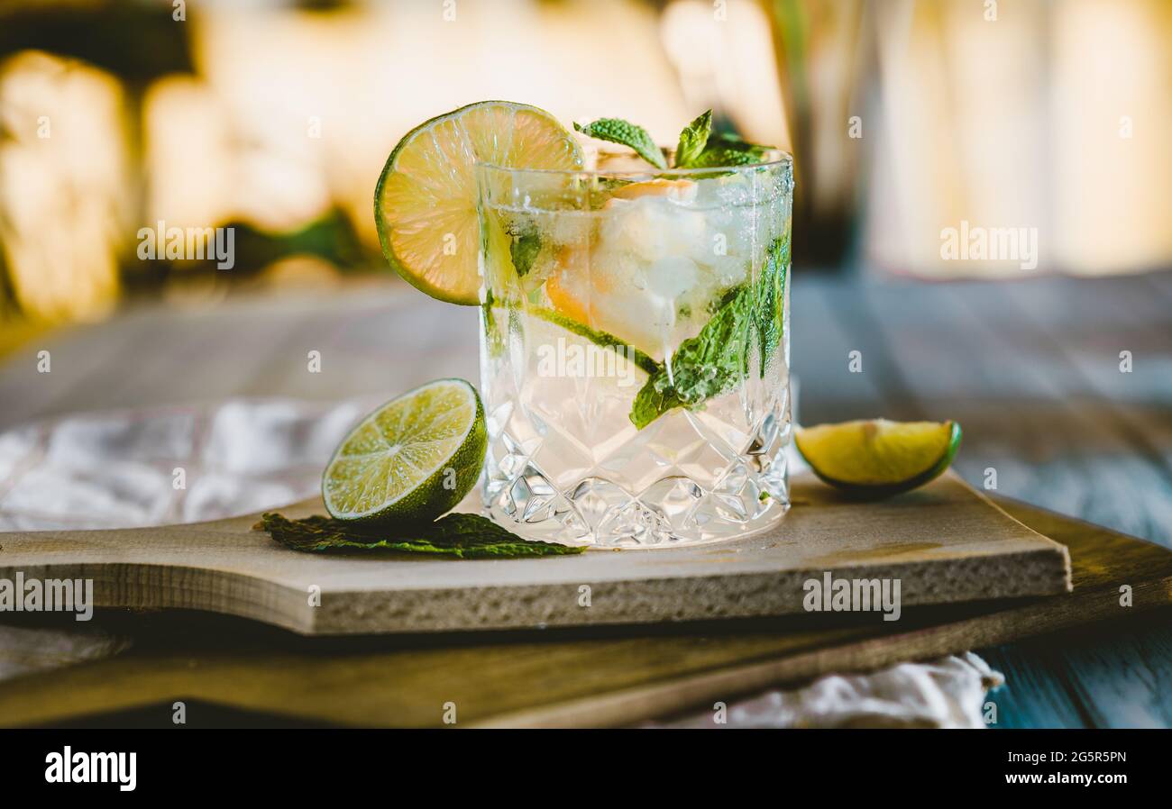 Moody fotografia scura di una bevanda fredda, un bicchiere di mojito con foglia di menta, ghiaccio, limone e zucchero su un tavolo di legno di stile vintage. Foto Stock