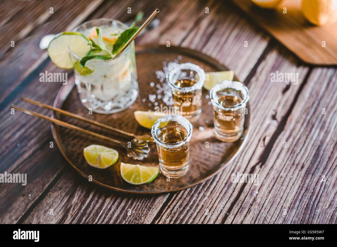 Fotografia scura di una bevanda fredda, un bicchiere di mojito con foglie di menta, ghiaccio, limone e zucchero con colpi di tequila su un tavolo di legno Foto Stock