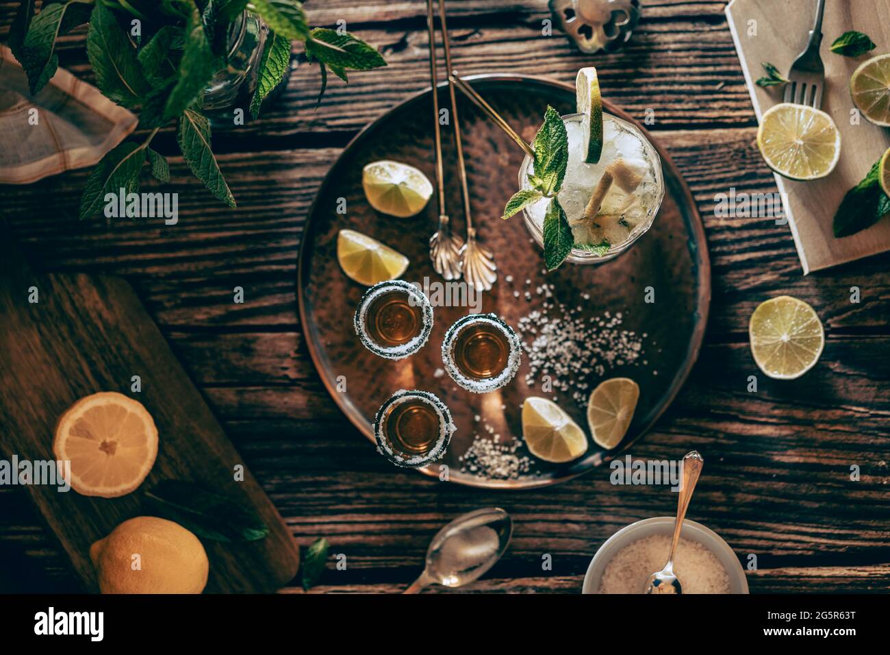 Fotografia piatta di una bevanda fredda, un bicchiere di mojito con foglie di menta, ghiaccio, limone e zucchero con colpi di tequila su un tavolo di legno Foto Stock