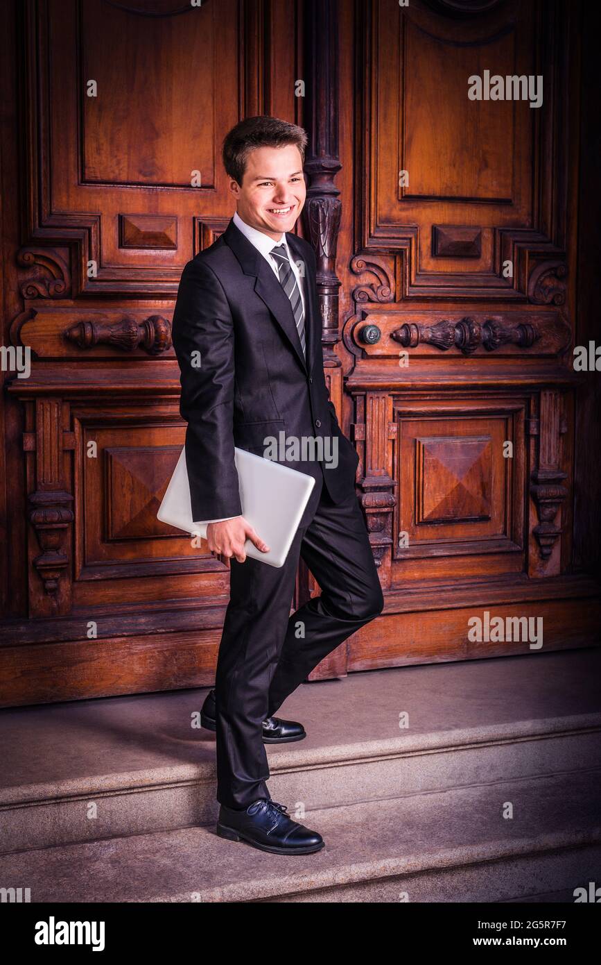 Vestendo formalmente in un vestito nero, una cravatta e una camicia bianca,  trasportando un computer portatile, un giovane studente universitario sta  camminando giù sulle scale dalla th Foto stock - Alamy