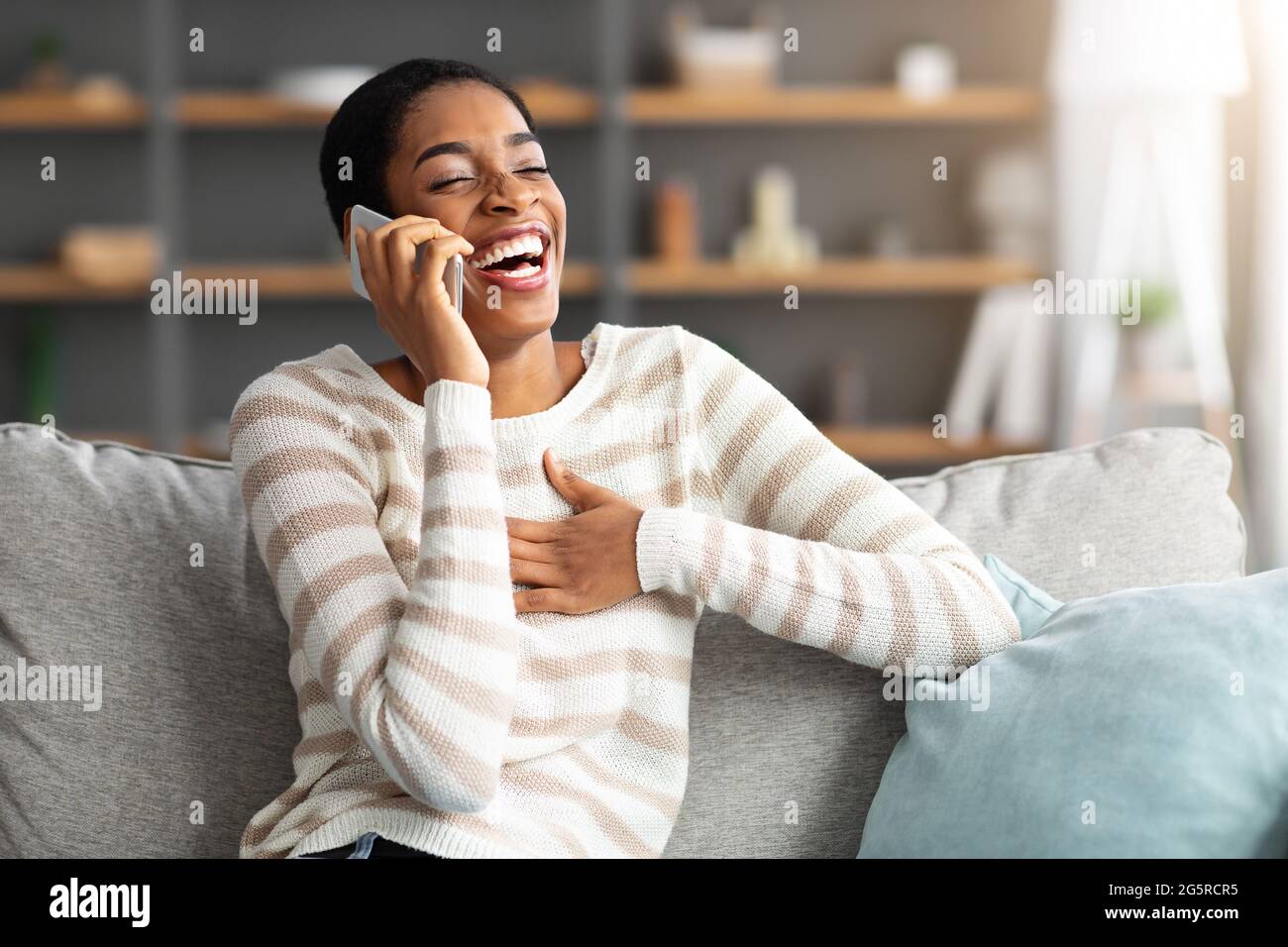 Piacevole chiamata. Allegra donna africana che si fa cattivere mentre si parla su Cellphone a casa Foto Stock