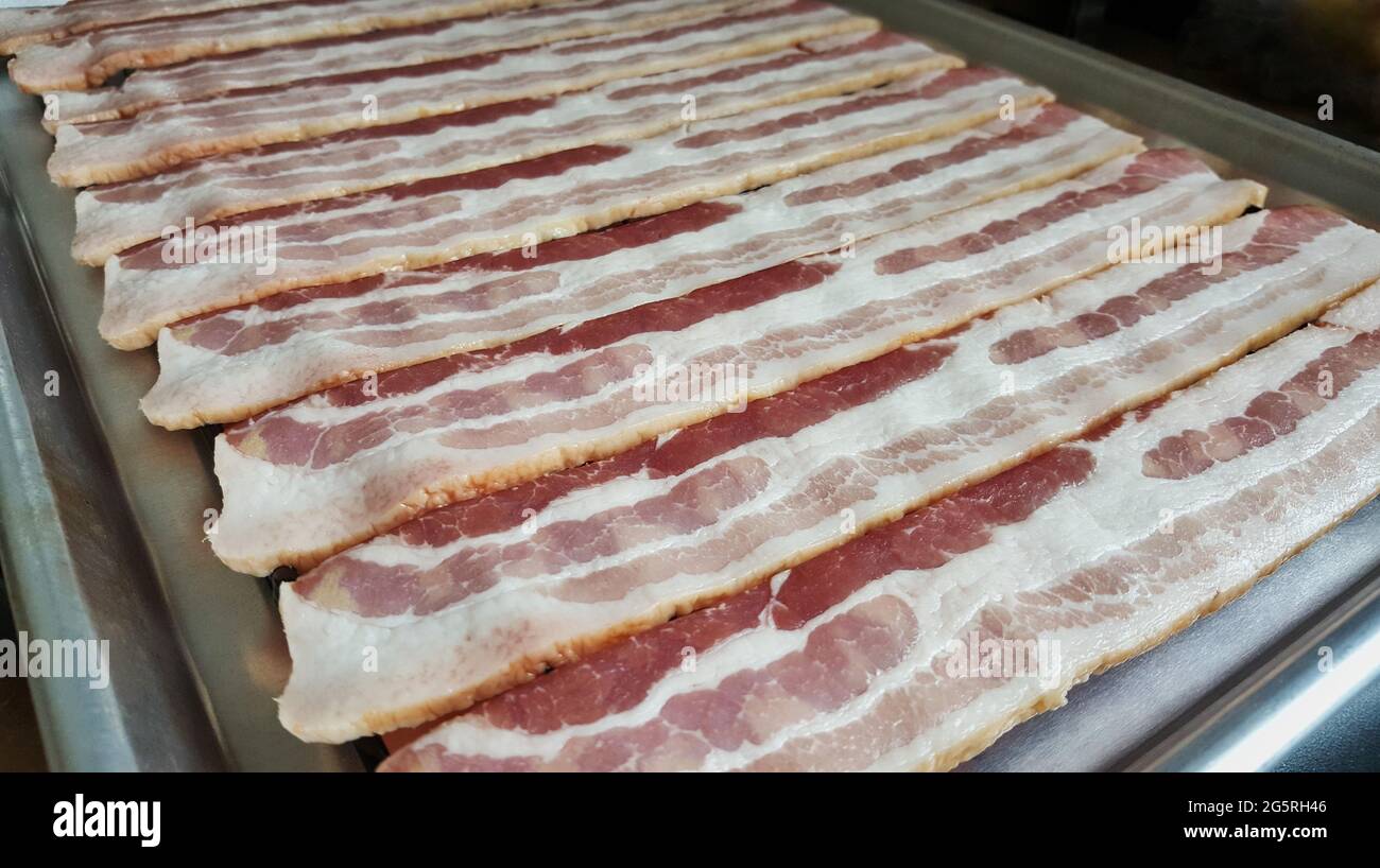 Strisce di pancetta grezza allineate su un forno rack, vista ad angolo basso con profondità di campo poco profonda e messa a fuoco in primo piano. Foto Stock