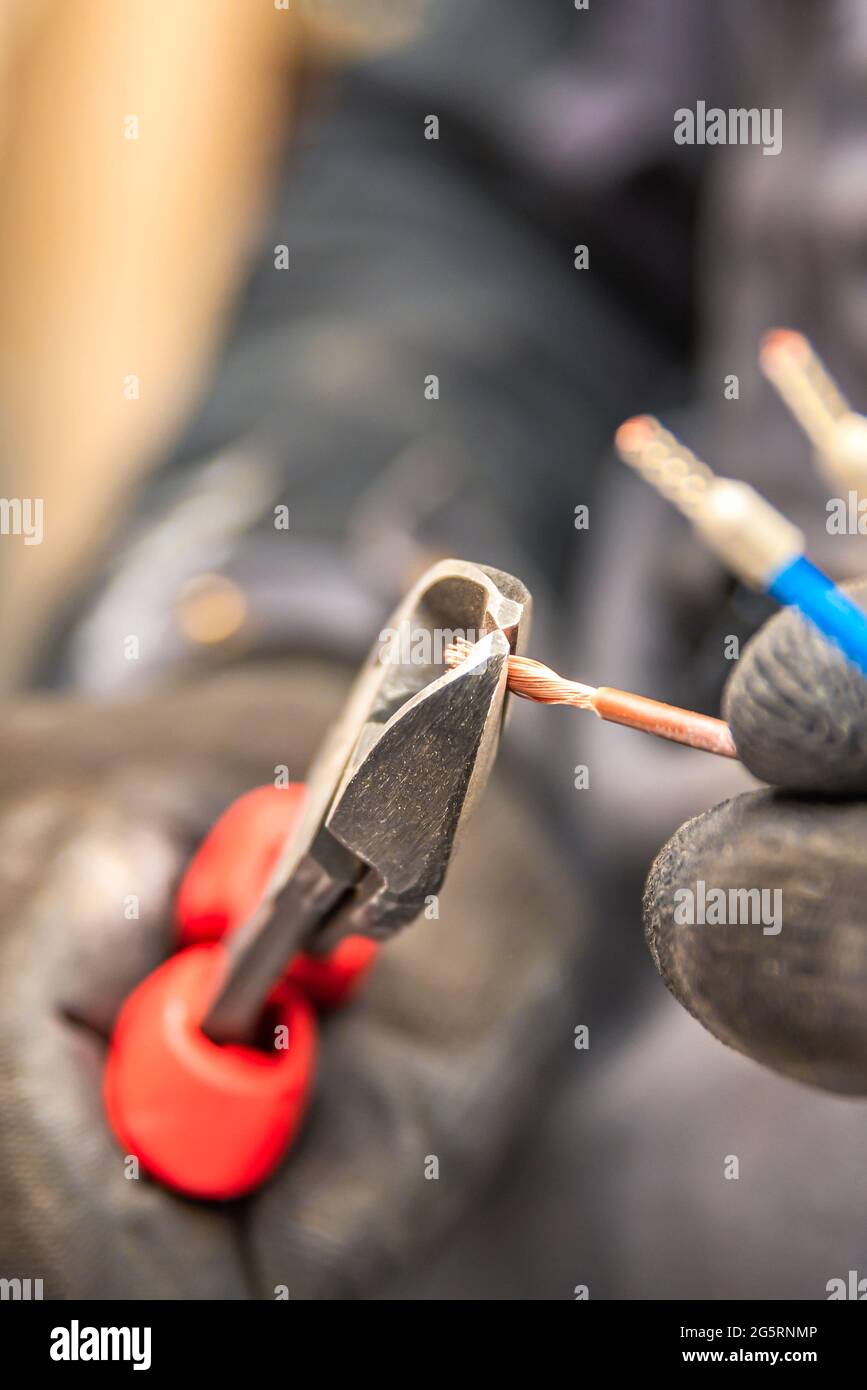L'elettricista taglia i cavi elettrici con le pinze, installa gli elettrodomestici, gli utensili per elettricisti. Foto verticale Foto Stock