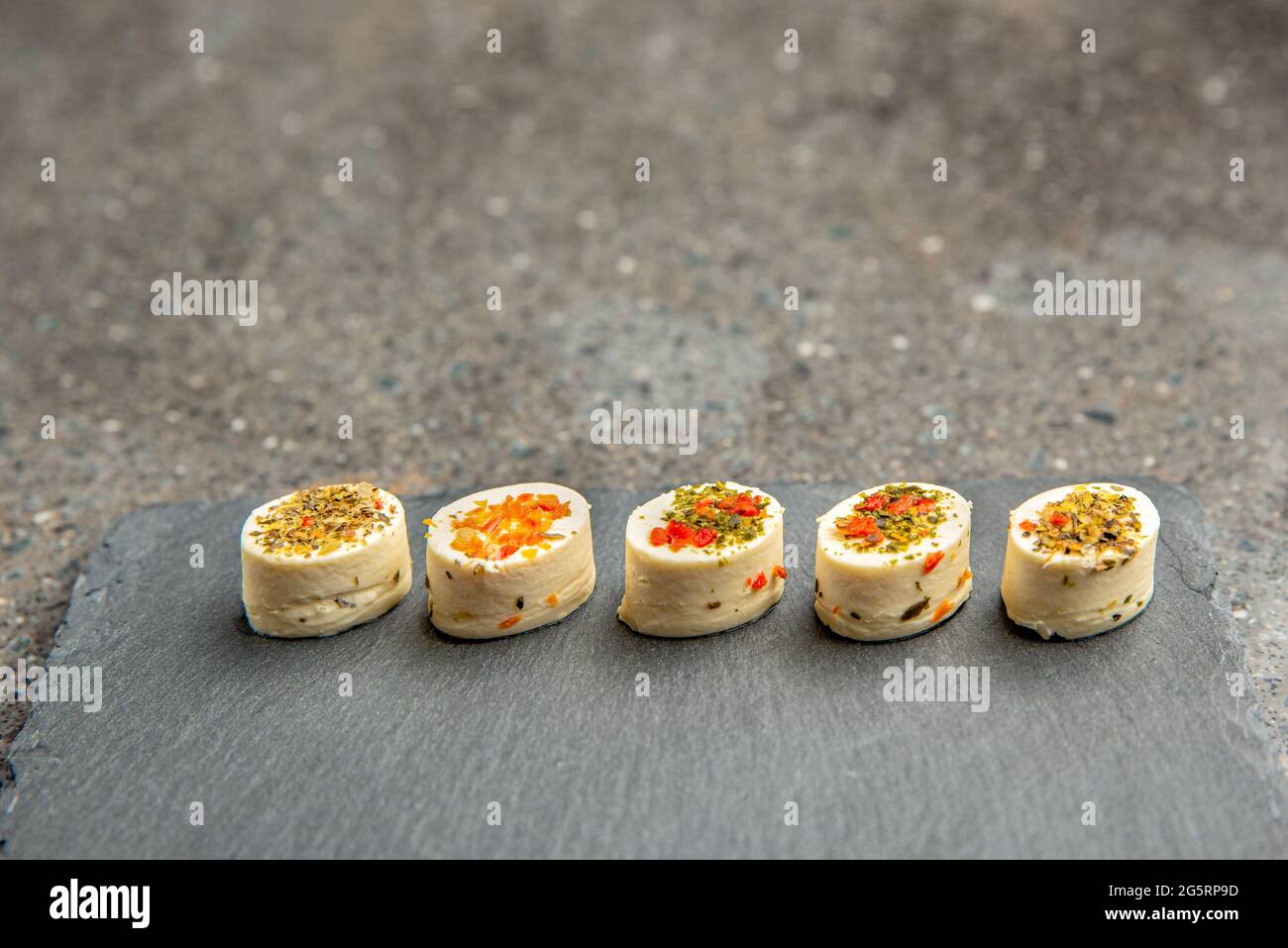 Piatto di formaggi con spezie. Mazzarella con spezie diverse. Spuntini di formaggio di vari sapori su un fondo nero del vassoio di pietra o banner sopra Foto Stock