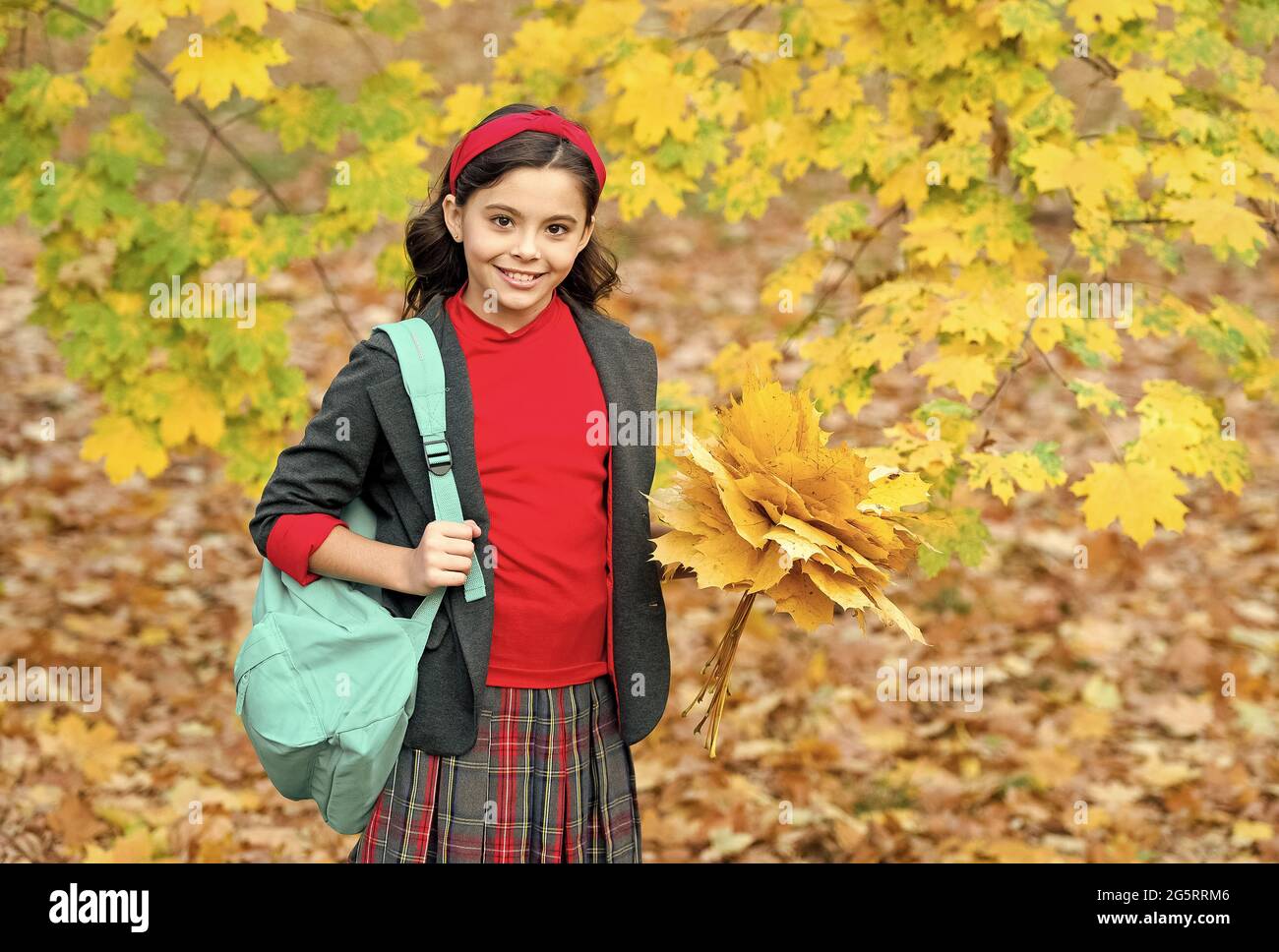 felice scuola ragazza manciata di foglie di acero giallo nel parco, tempo di scuola Foto Stock