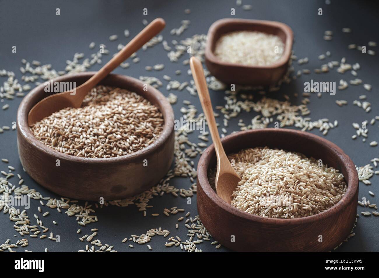 Set di diversi tipi di riso e cereali nelle ciotole di legno e un cucchiaio di bambù Foto Stock