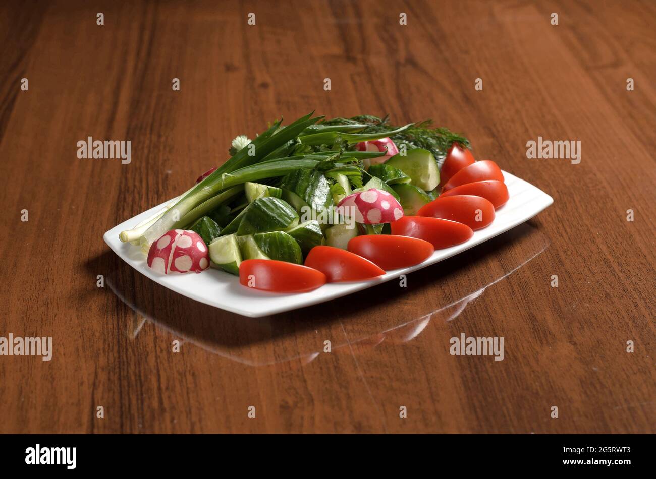 Verdure fresche tritate, pomodori, cetrioli, rafano, cipolla, aneto, prezzemolo in un piatto sulla tavola, verdure assortite Foto Stock