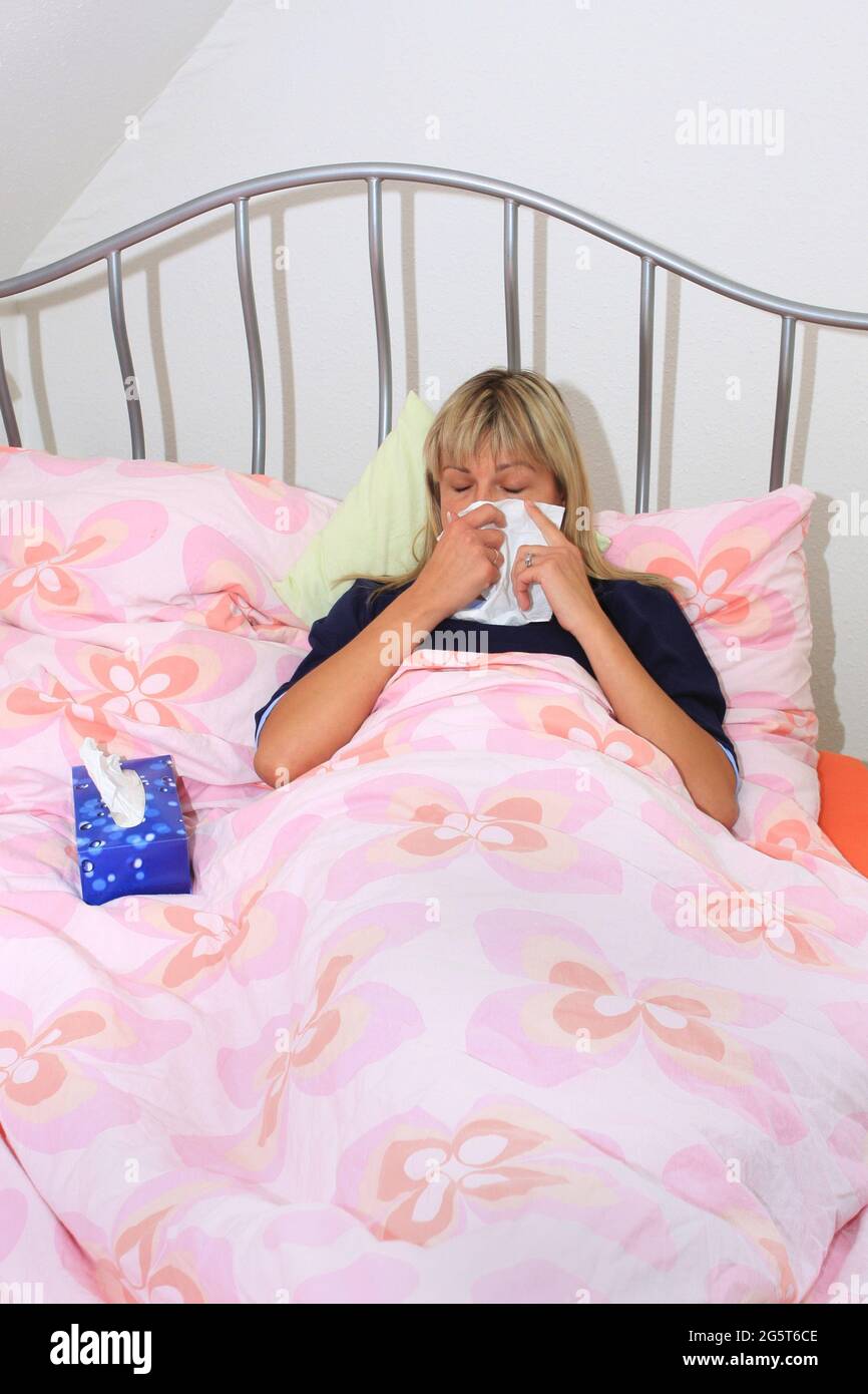 la donna si trova a letto con un freddo e soffia il naso Foto Stock