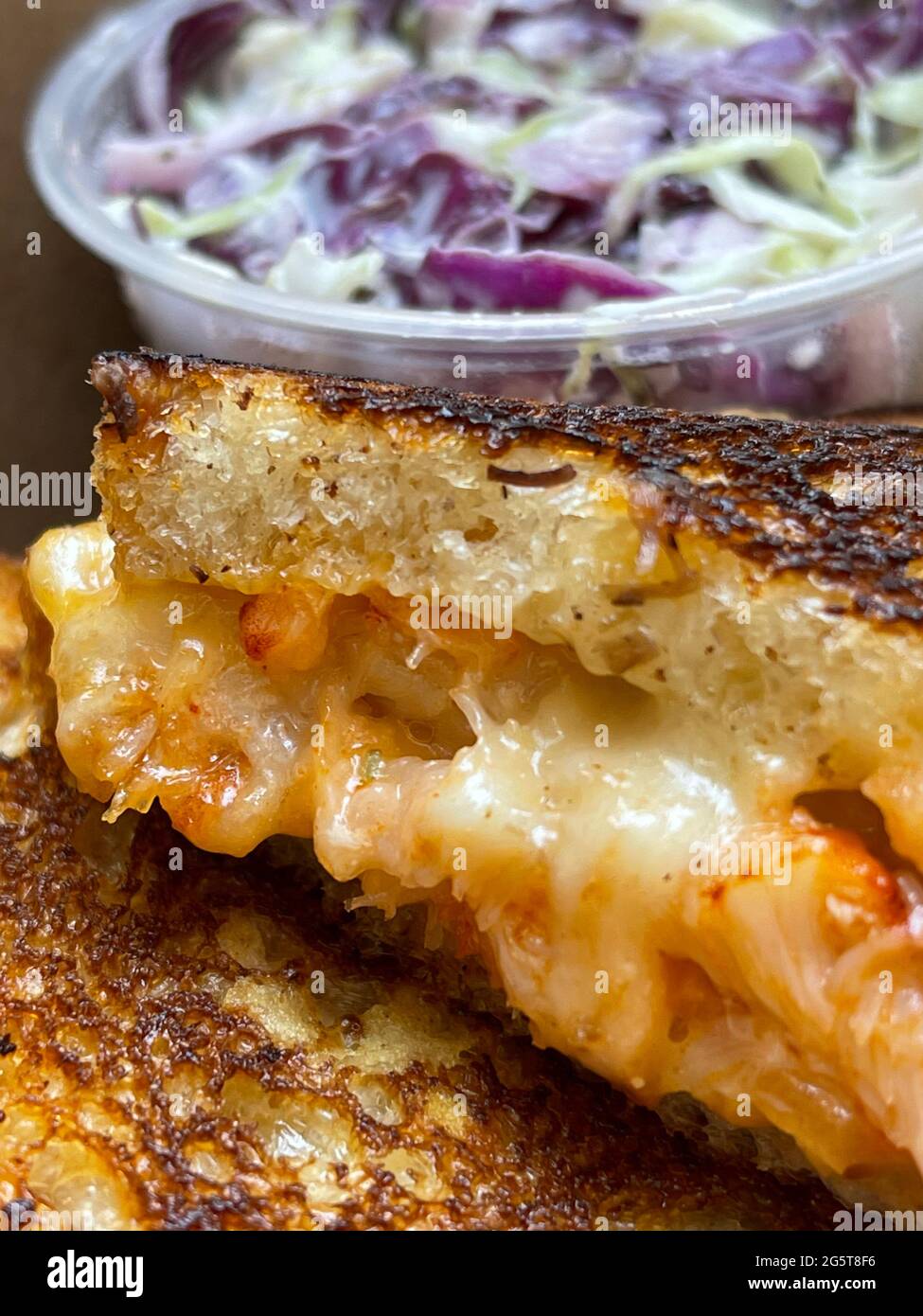 Primo piano di un sandwich al formaggio alla griglia con formaggio fuso e un lato di crema di insalata di cavolo in un contenitore di plastica Foto Stock