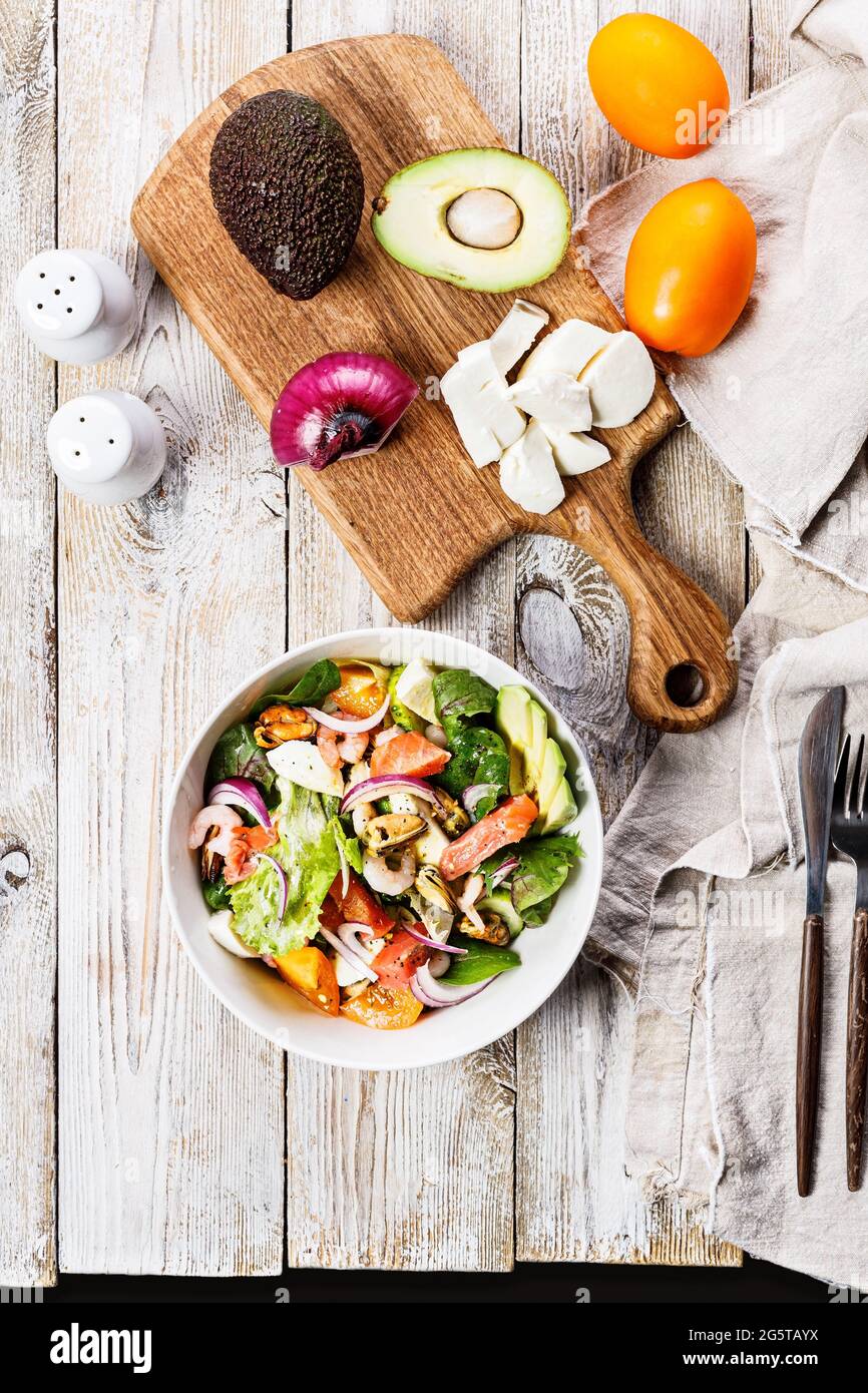 Insalata estiva mediterranea a shot verticale. Cozze, gamberetti, salmone, pomodori, insalata di ghiaccio, Avocado, cipolla, bietole svizzere e olio d'oliva. Ancora vita di seafo Foto Stock