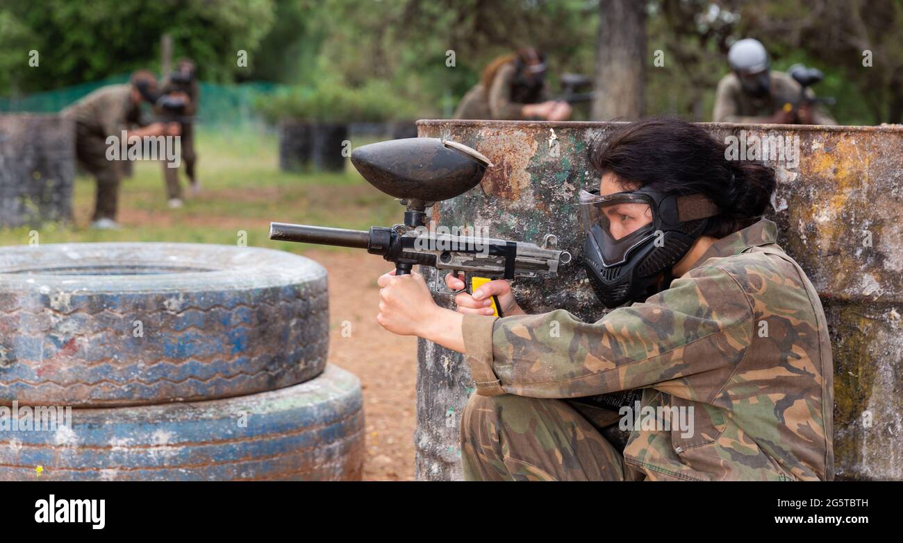 Giocatore di paintball femminile in camouflage e maschera di mira con pistola in shootout Foto Stock