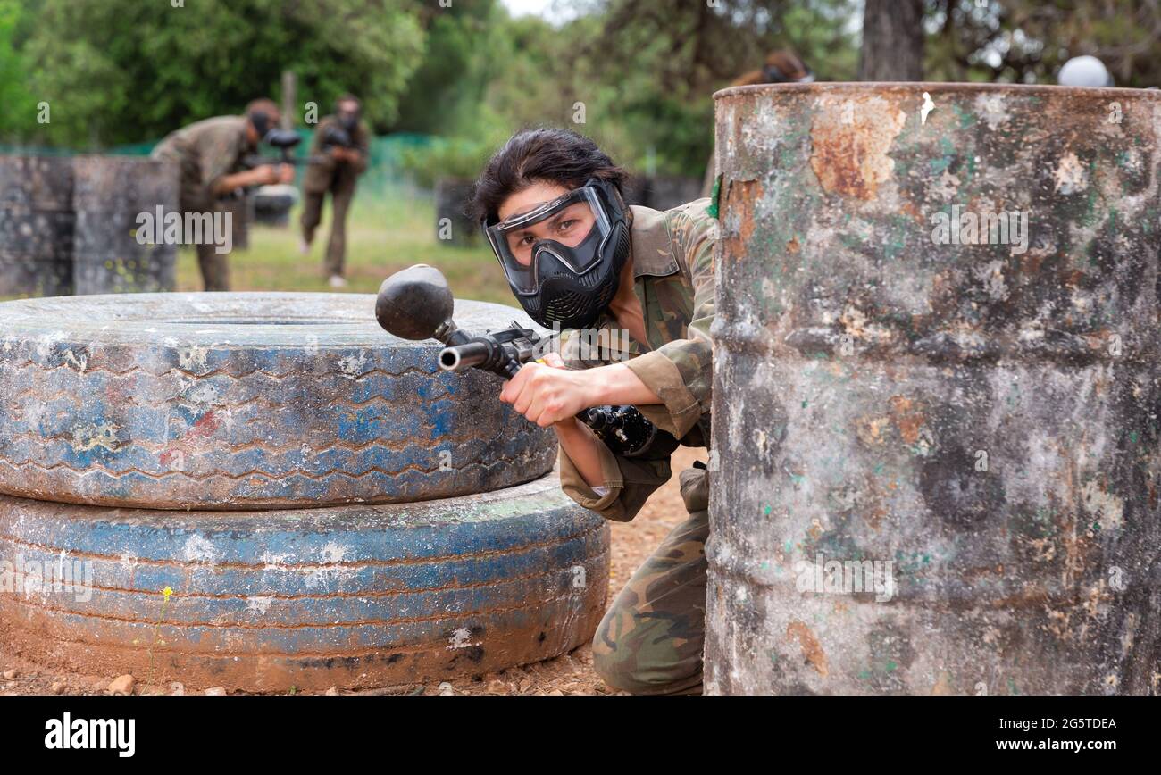 Giocatore di paintball femminile in camouflage e maschera di mira con pistola in shootout Foto Stock