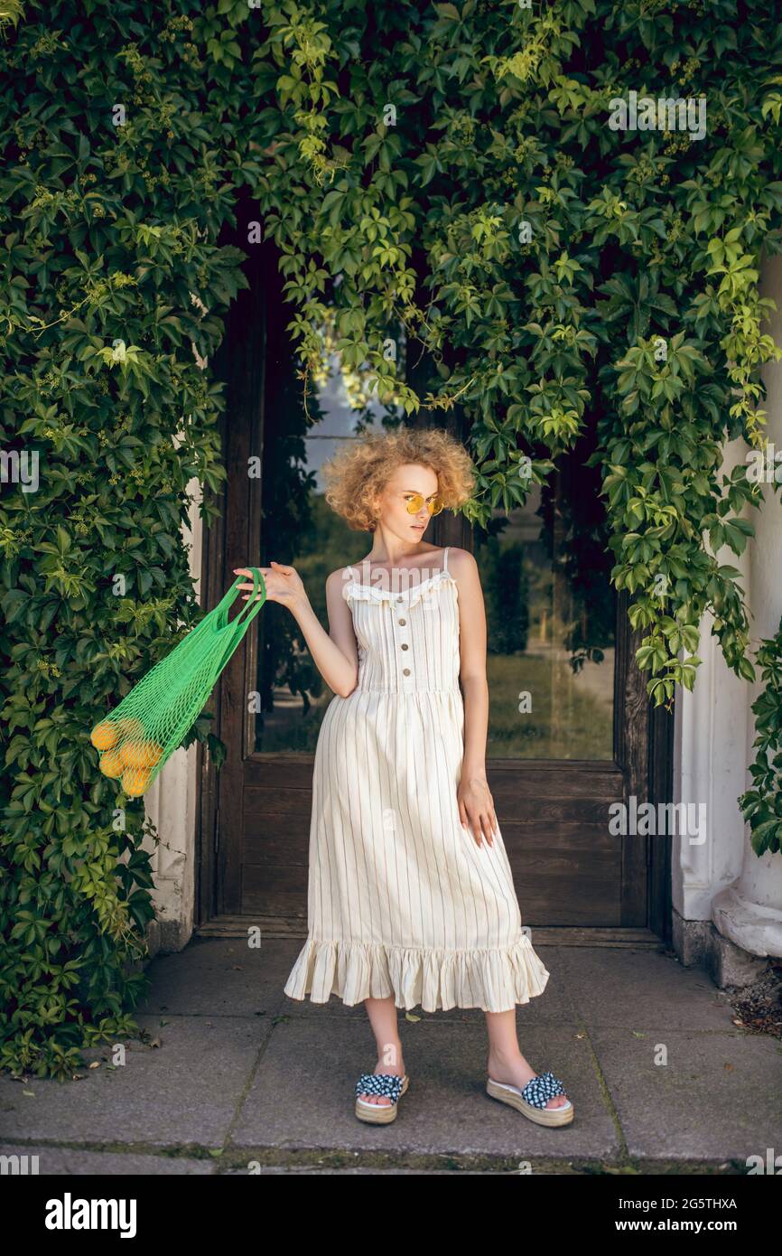Giovane donna in un vestito bianco lungo che tiene una borsa di maglia  verde nelle sue mani Foto stock - Alamy
