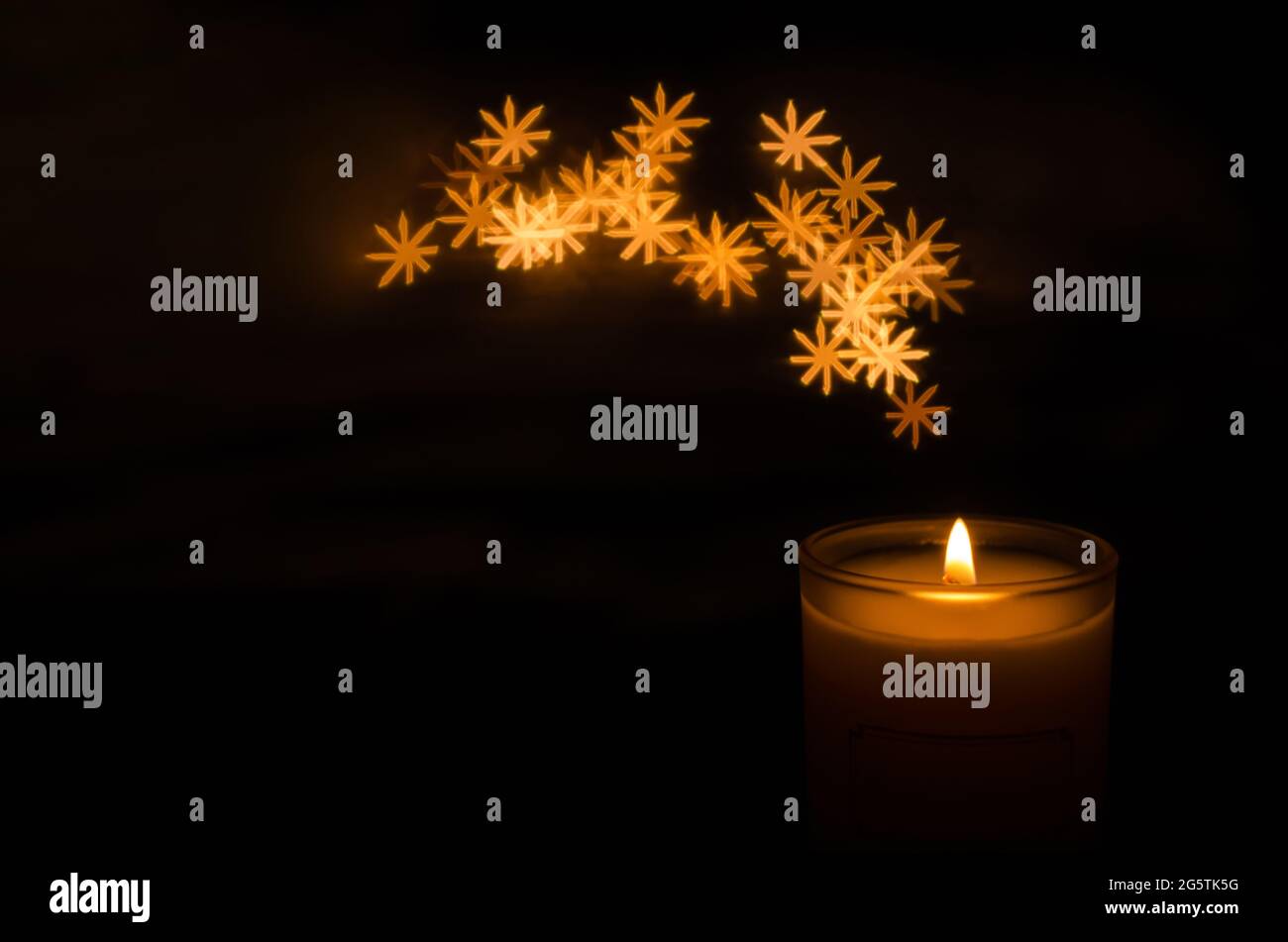 Candela aromatica con fiamma e fiocco di neve forma bokeh su sfondo scuro per ringraziamento e giorno di Natale. Foto Stock