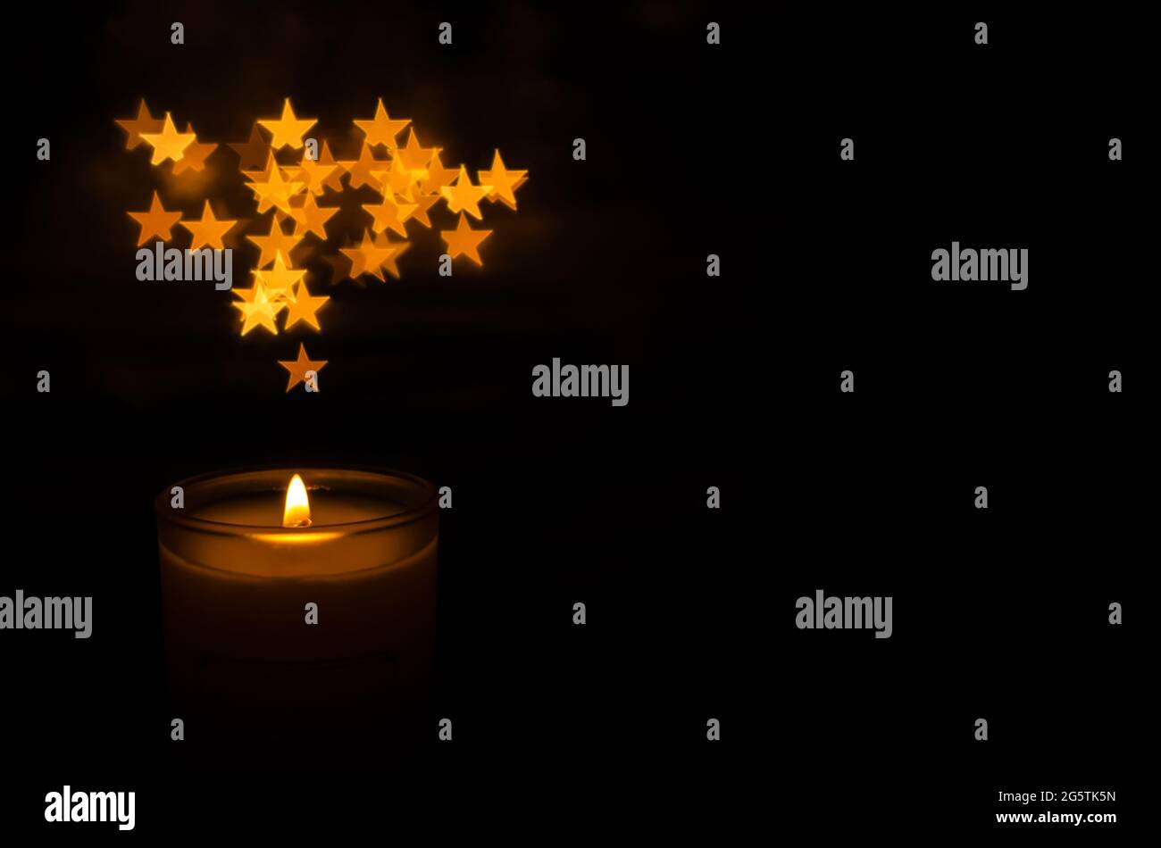 Candela aromatica con fiamma e bokeh a forma di stella su sfondo scuro per ringraziamento e giorno di Natale. Foto Stock