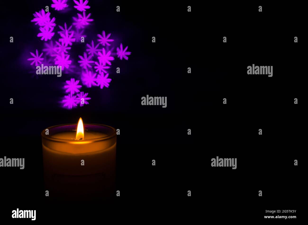 Candela aromatica con fiamma e fiocco di neve forma bokeh su sfondo scuro per ringraziamento e giorno di Natale. Foto Stock