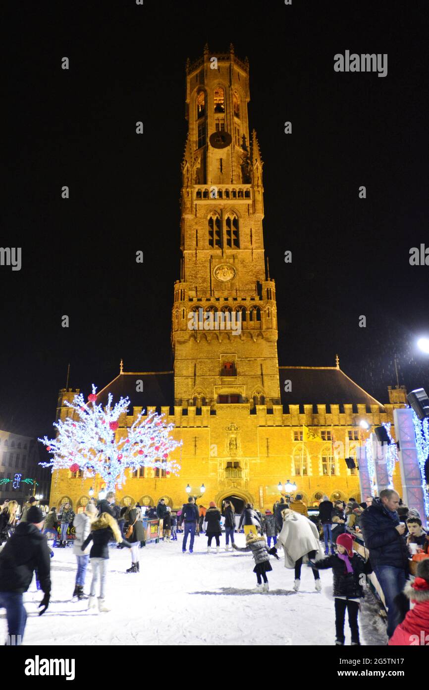 BELGIO. FIANDRE. BRUGES A NATALE. PISTA DI PATTINAGGIO SU GHIACCIO SUL GRAND PLACE CON IL CAMPANILE DI NOTTE. Foto Stock