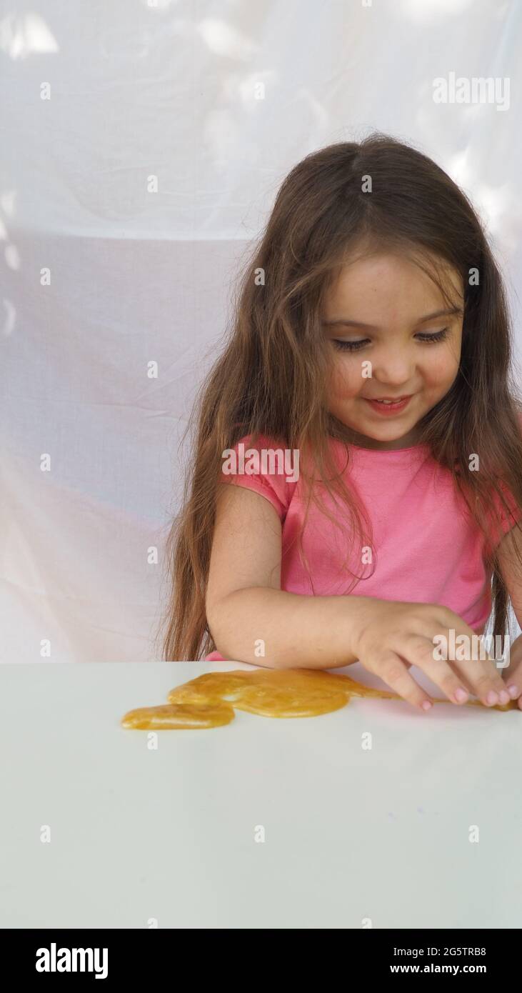 Kid Playing Hand Made Toy chiamato Slime. Ragazza carina in una t-shirt rosa gioca con un giallo slime. Creatività contemporanea. Stretching, scamming, modellazione Foto Stock