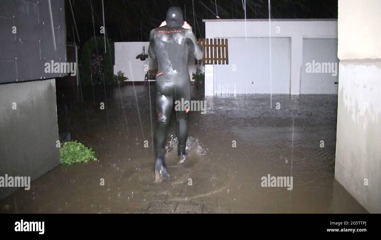 Essen, Germania. 30 giugno 2021. Un uomo viene dal garage durante la tempesta in un vestito da immersione in neoprene - vuole aiutare un vicino. La pioggia battente aveva allagato giardini, cantine e garage. Credit: Markus Gayk/Telenewsnetwork/dpa/Alamy Live News Foto Stock