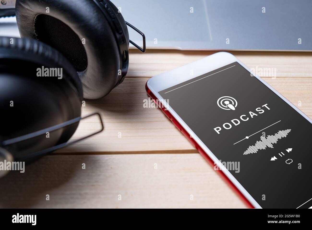 Primo piano di uno smartphone che riproduce un podcast, con auricolari, su un tavolo. Audience podcast Foto Stock