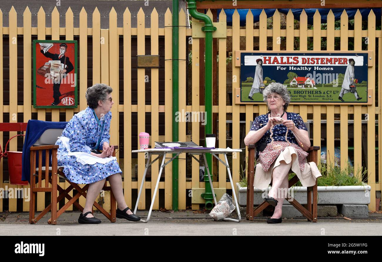 Due donne anziane negli anni '40 si stancano sulla stazione ferroviaria di Alresford durante l'evento annuale War on the Line, Alresford, Hampshire, Regno Unito. 13 giugno 2021. Foto Stock