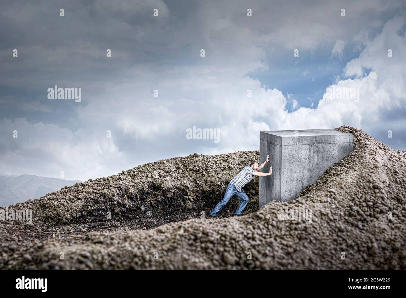l'uomo spinge un enorme cubo di cemento strisciando nel terreno. concetto di determinazione e forza. Foto Stock