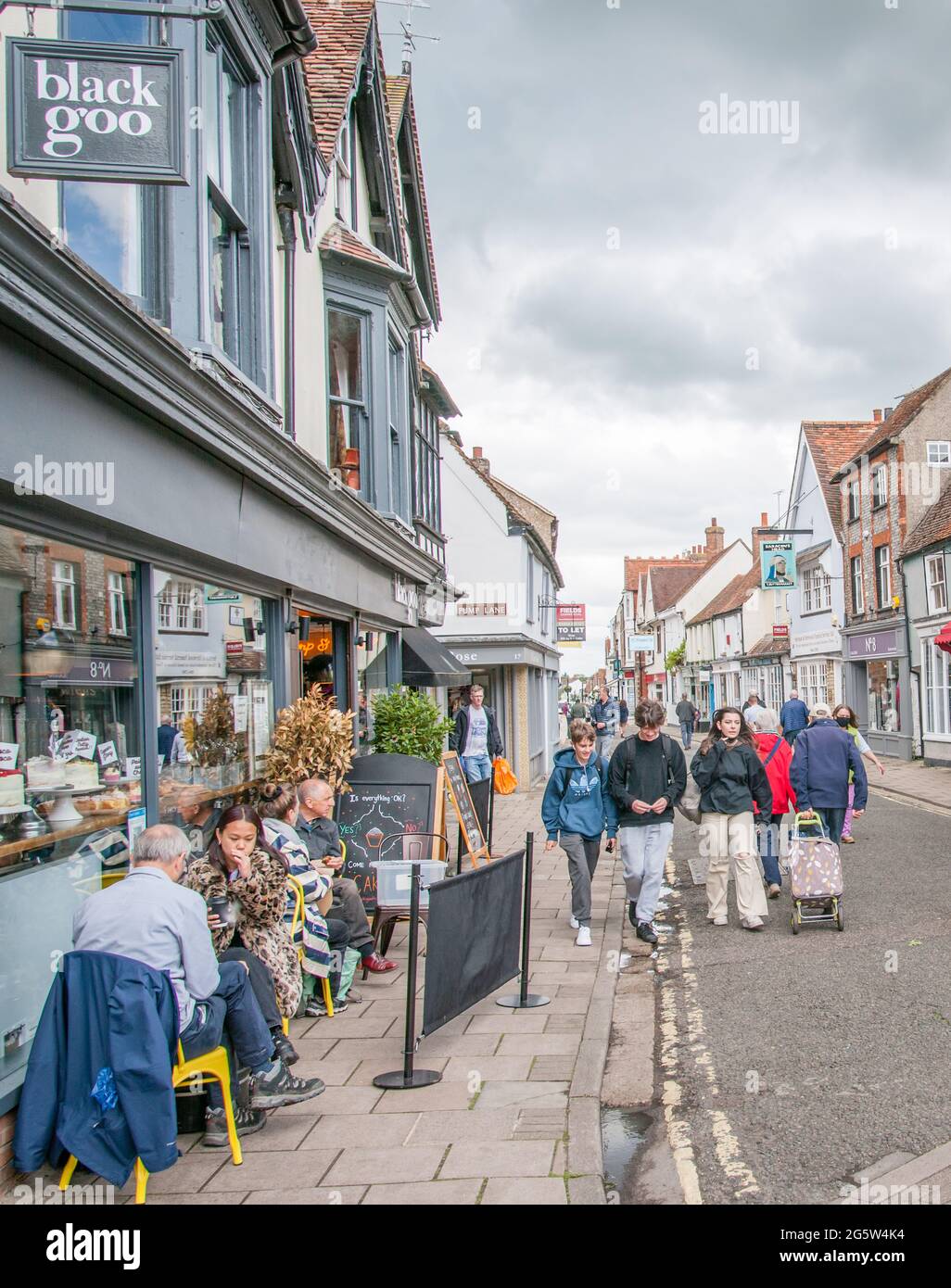 Un gruppo di giovani che passeggiano per il Buttermarket, Thame, Oxfordshire. Mentre altri godono un caffè all'aperto. Foto Stock