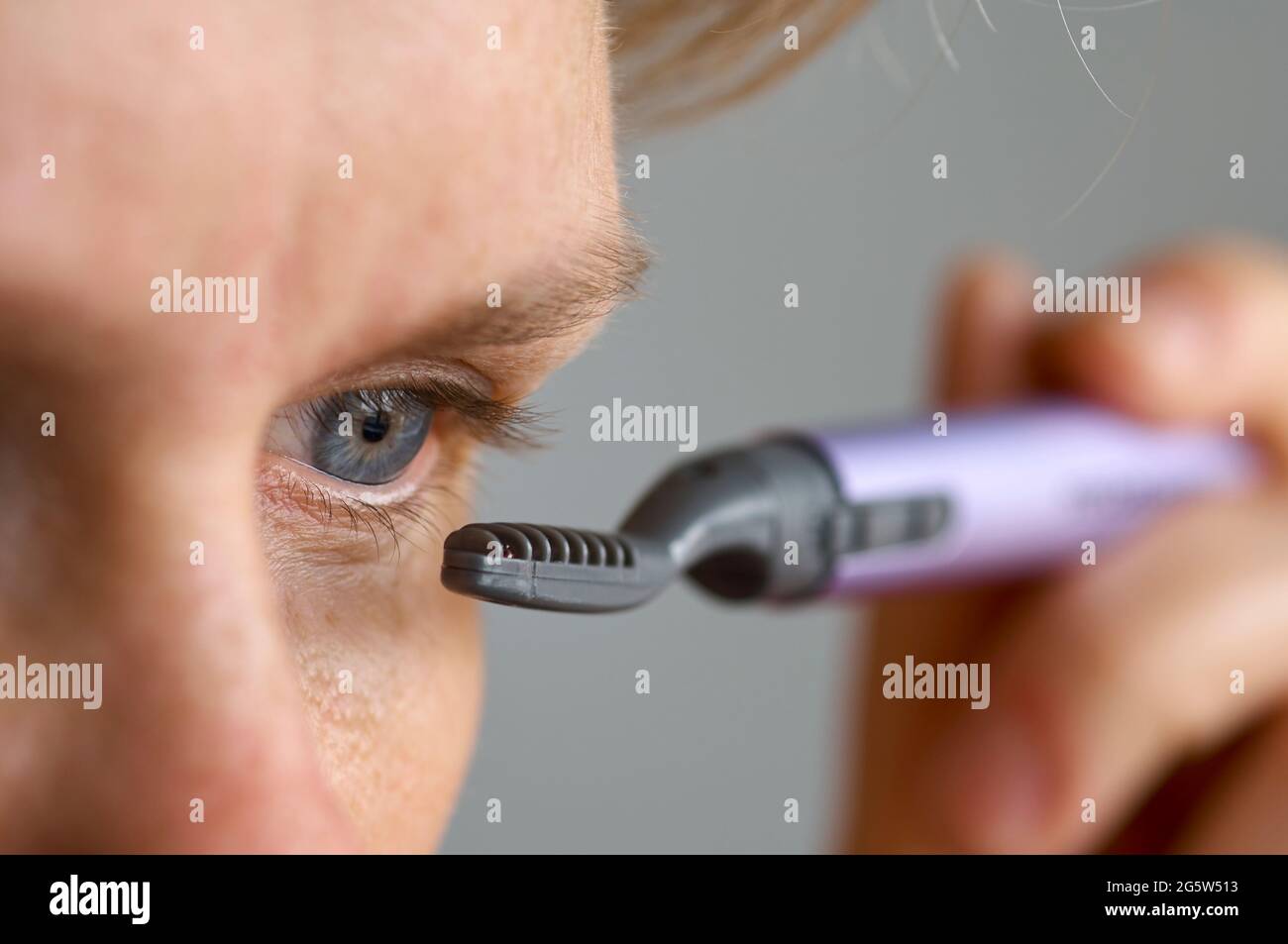 giovane caucasica modello femminile reale con occhi blu utilizzando un arricciacapelli portatile elettrico riscaldato eyelash primo piano Foto Stock