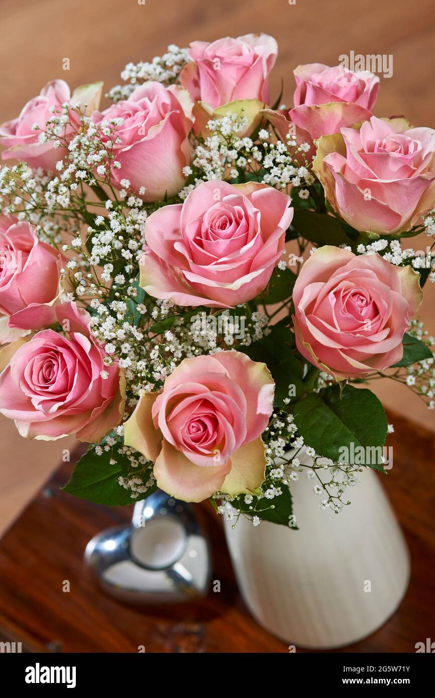 Bouquet misto di rose rosa morbide e gypsofila in un vaso su un tavolino da caffè in un ambiente domestico Foto Stock