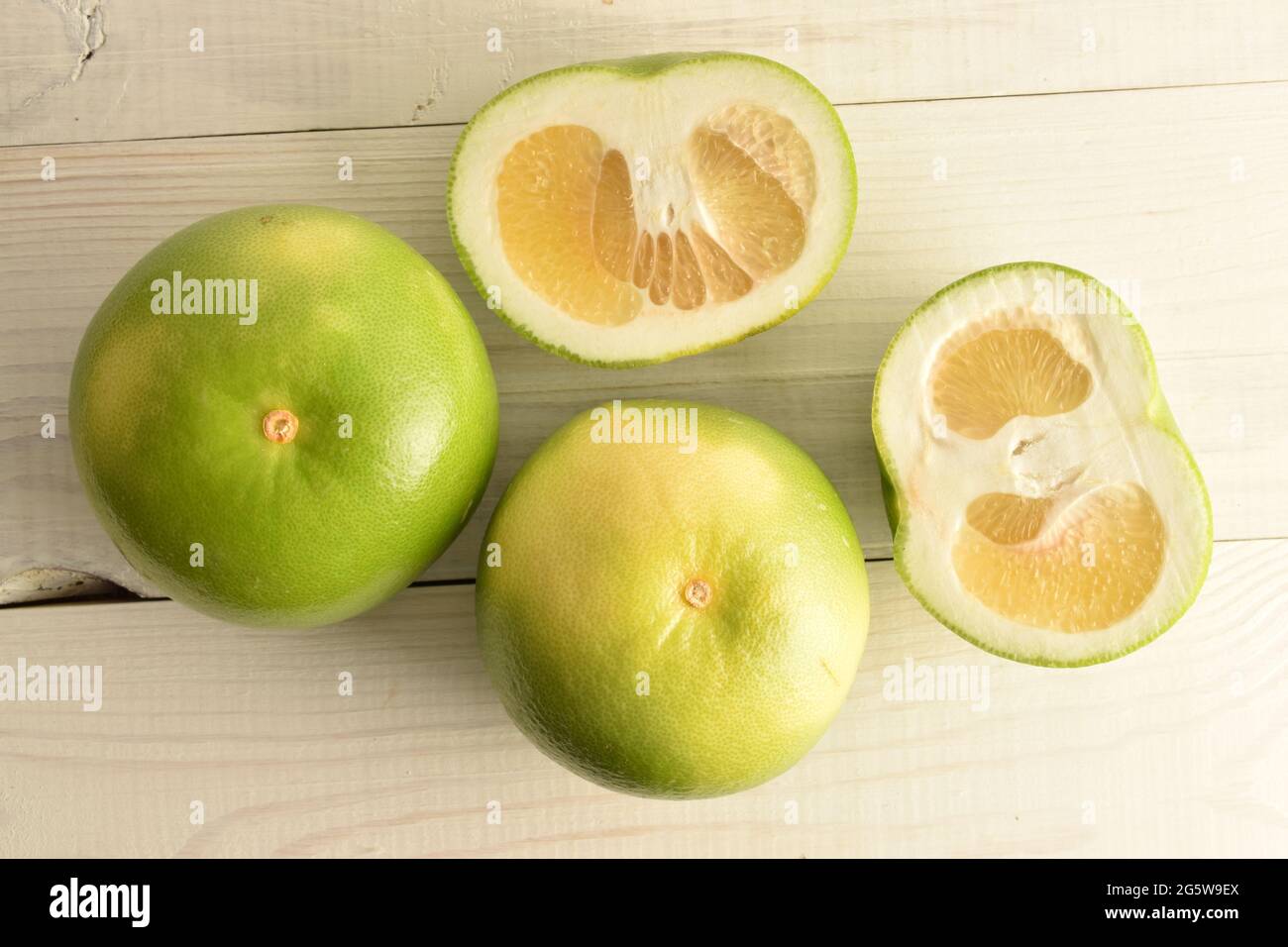 Due interi e due semi naturali Citrus Sweetie, primo piano, su un tavolo di legno bianco, vista dall'alto. Foto Stock