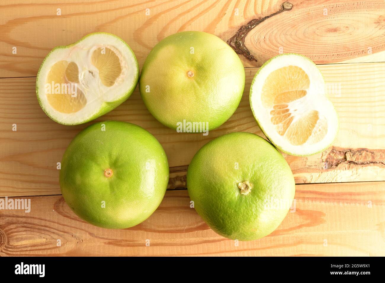 Tre interi e due semi naturali Citrus Sweetie, primo piano, su un tavolo di legno, vista dall'alto. Foto Stock