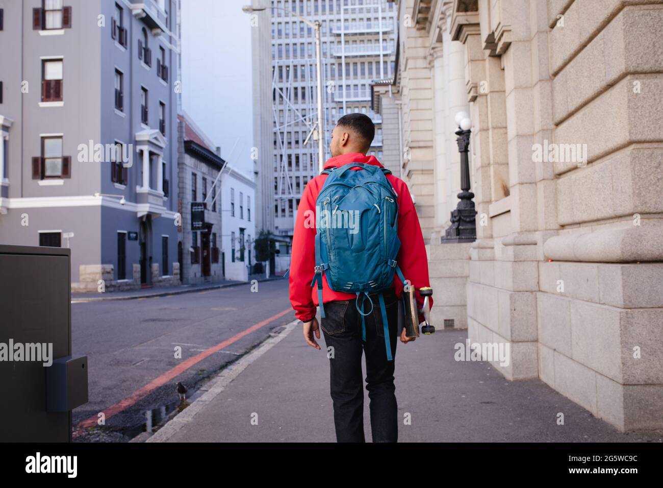 Vista posteriore di un uomo da corsa misto con zaino e skateboard che  cammina nella strada della città Foto stock - Alamy