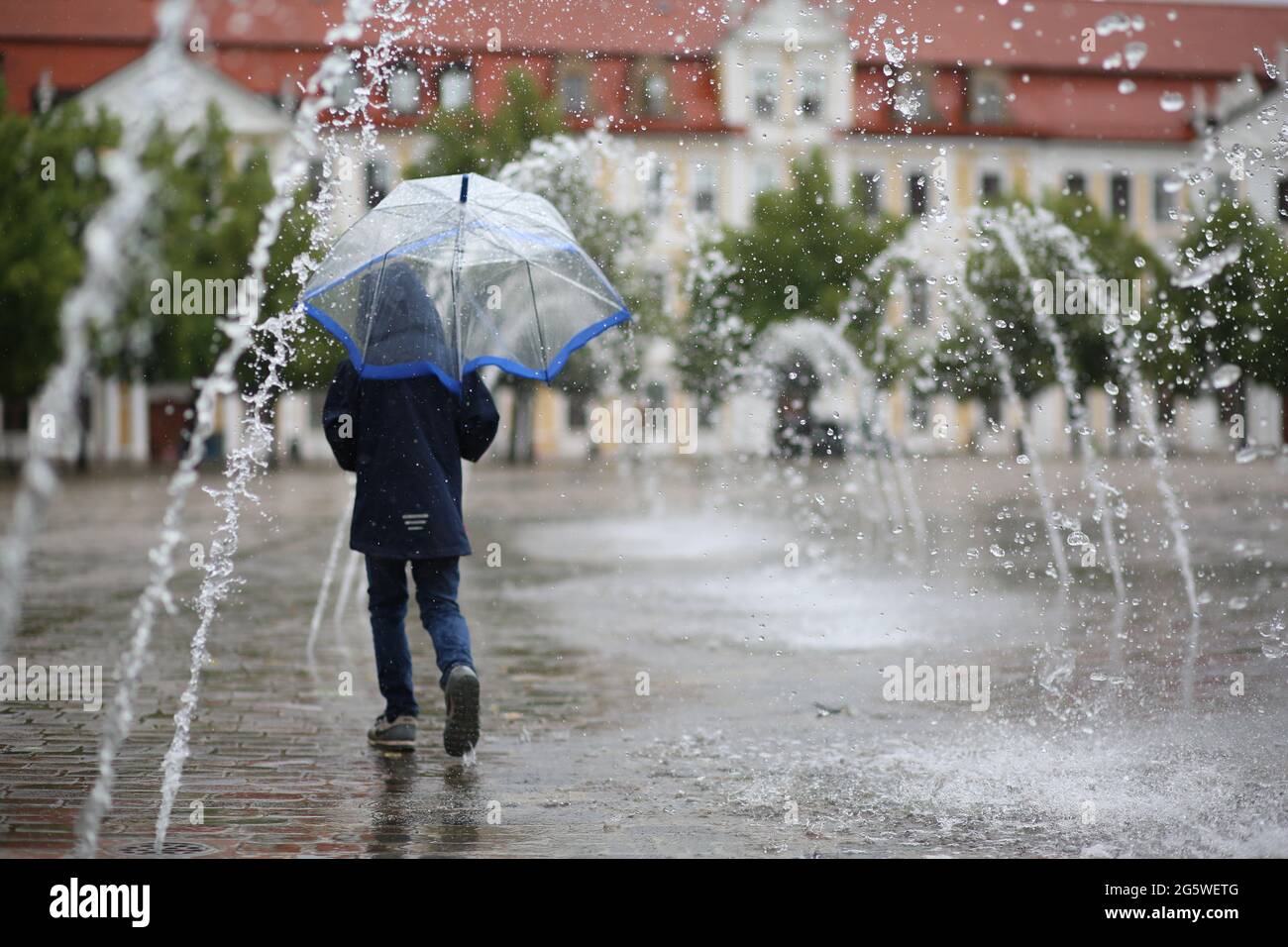 Magdeburgo, Germania. 30 giugno 2021. Un bambino cammina con un cartello attraverso una caratteristica acquatica sulla Piazza della Cattedrale in tempo piovoso. Nella capitale dello stato si sono tenute forti piogge continue. Credit: Matrhias Bein/dpa-Zentralbild/dpa/Alamy Live News Foto Stock