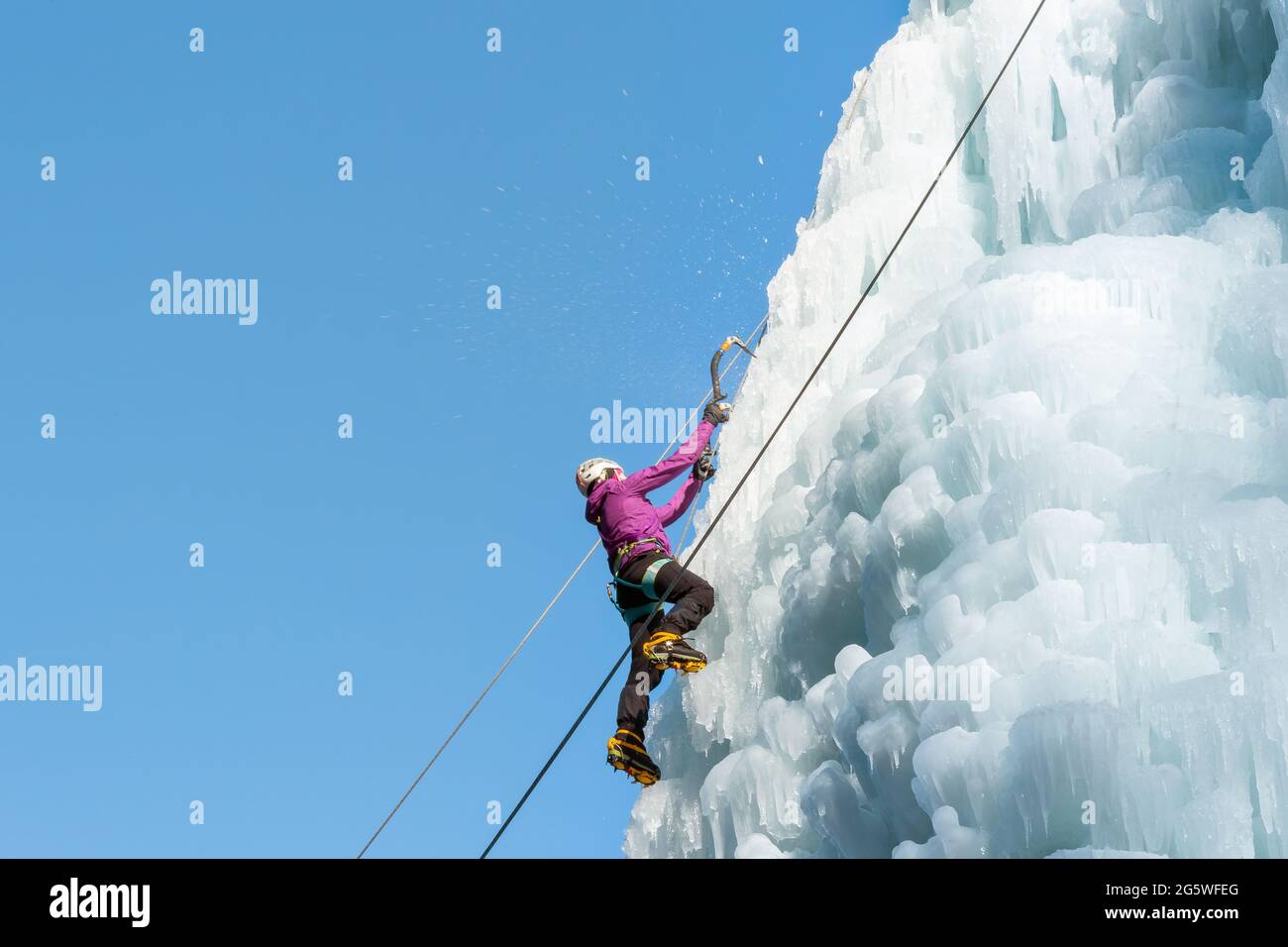 Arrampicata femminile su ghiaccio sul lato di un pendio ghiacciato con dossi, creste e iciclette Foto Stock