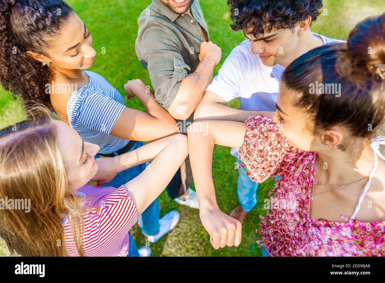 Cinque amici multirazziali in cerchio che batte gomito che si salutano a vicenda per il rispetto sociale di distanza in tempo pandemico. Nuove abitudini umane normali per C Foto Stock