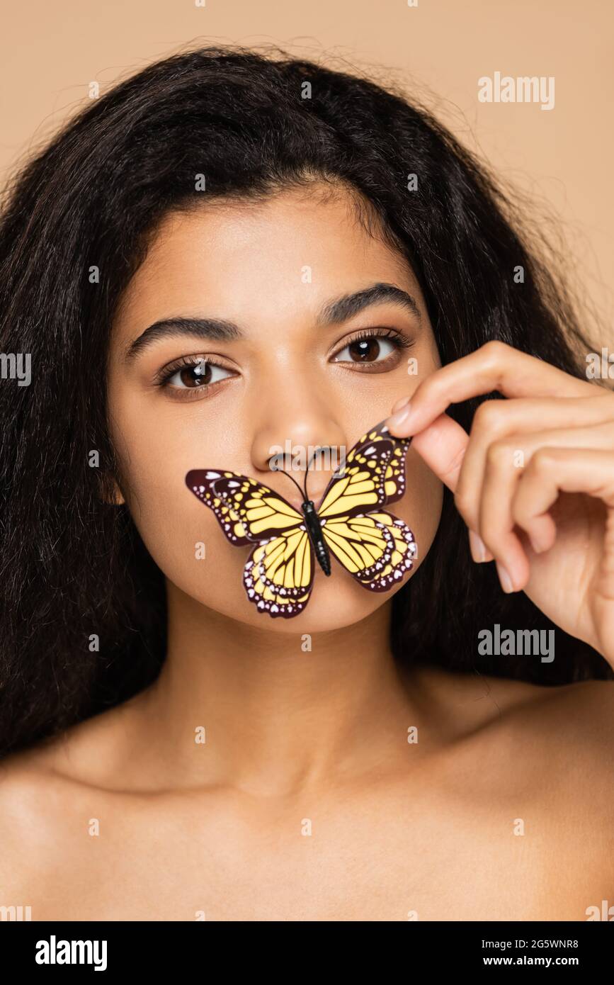 giovane donna afroamericana che tocca farfalla su labbra isolate su beige Foto Stock