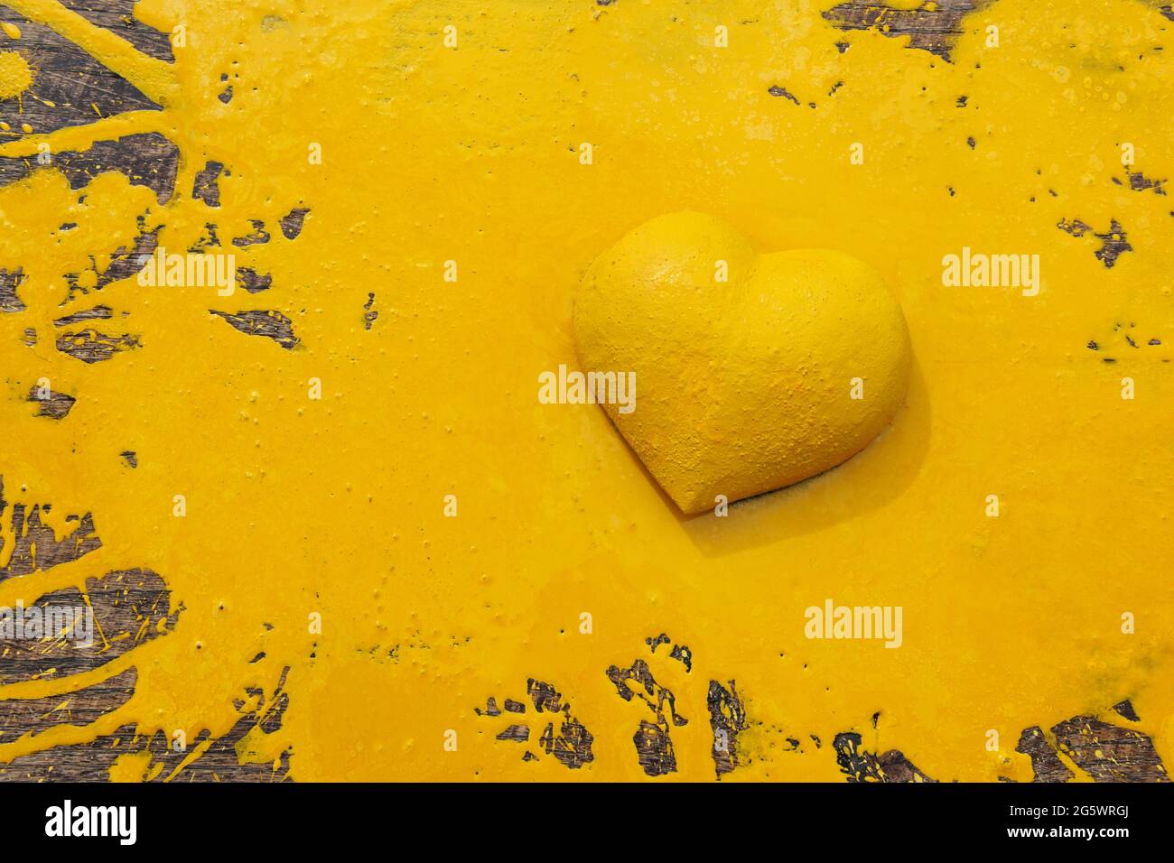 Erietta gialla. Forma tridimensionale del cuore su tavola in legno naturale frantumata da vernice gialla. Foto Stock