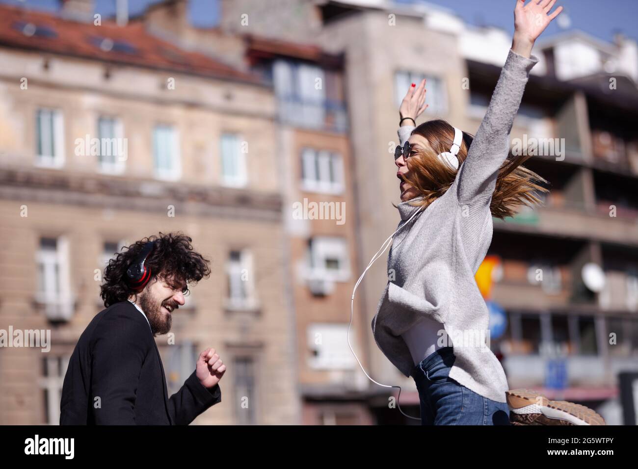 Giovani colleghi di lavoro che ballano insieme con le cuffie dopo il lavoro. Amici felici che saltano e si ingannano all'aperto. Foto Stock