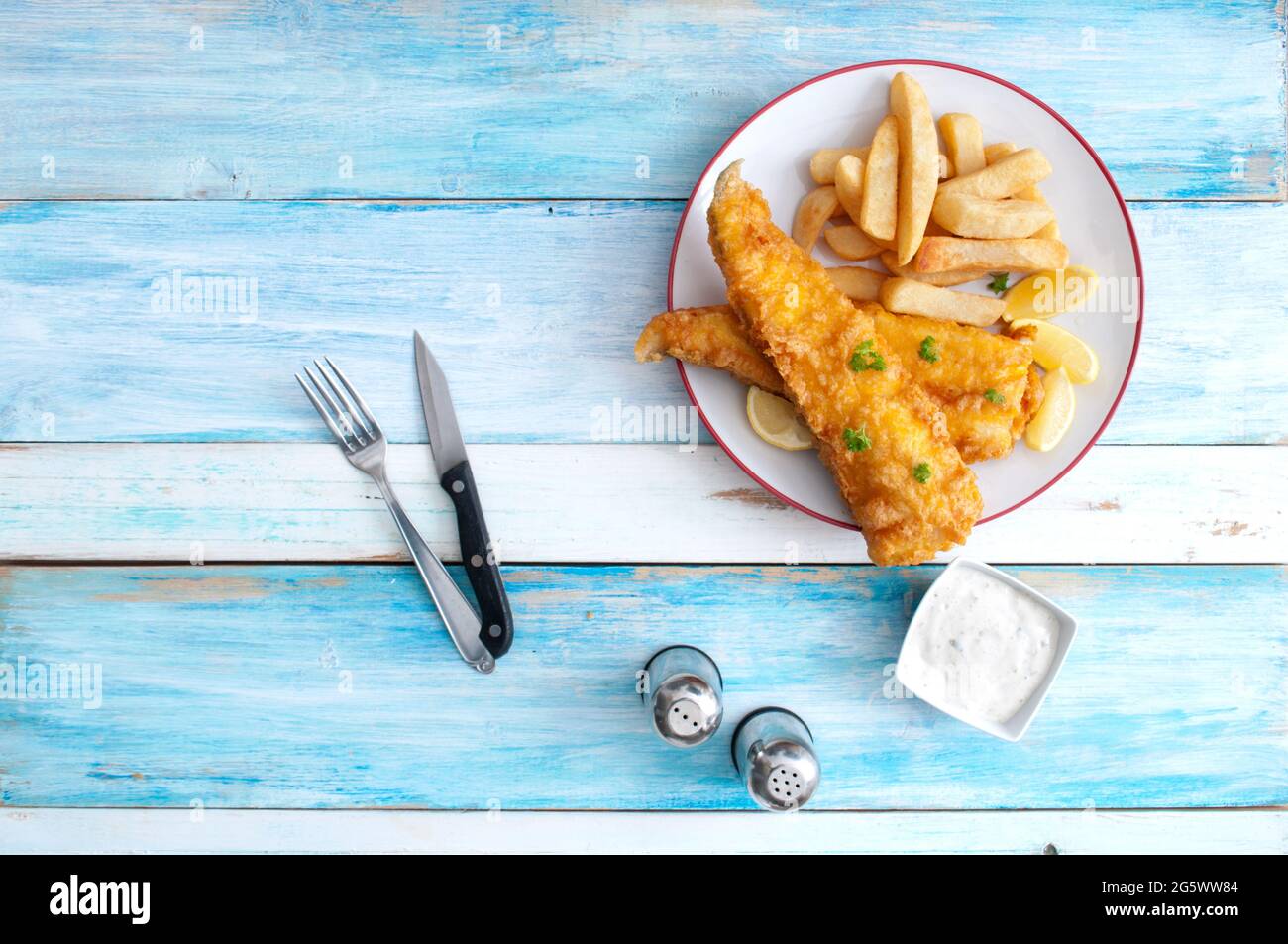 Pesce tradizionale e patatine su un piatto su tavola rustica in legno Foto Stock
