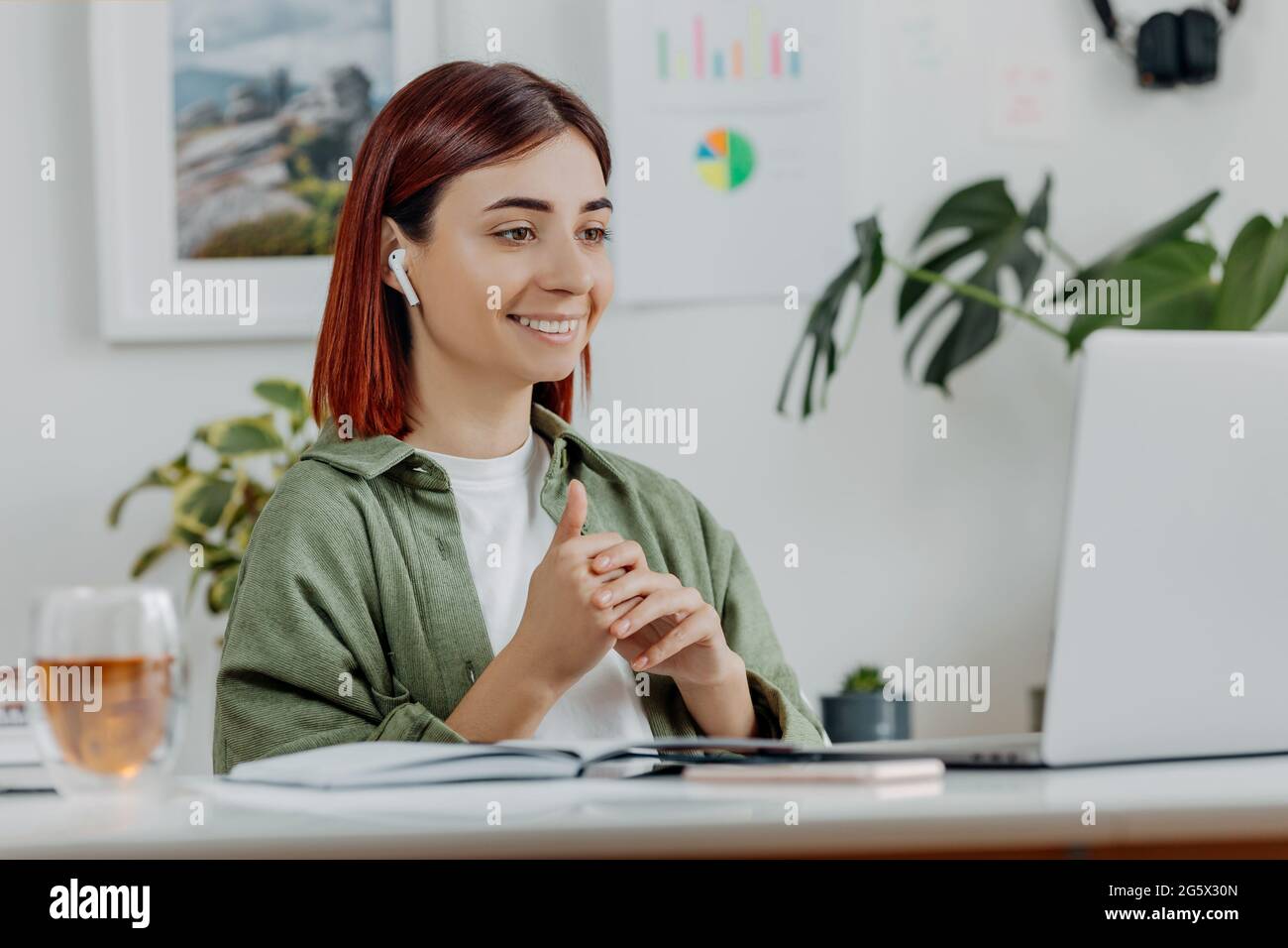 Donna che lavora in remoto a casa con un computer portatile. Giovane donna d'affari che parla con gli auricolari wireless. Concetto di business online o di comunicazione, freelance Foto Stock