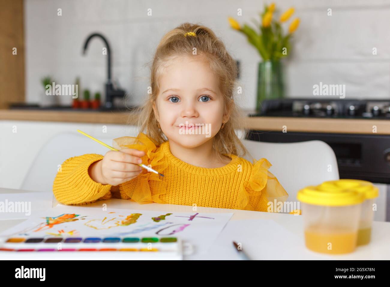 Carino bambina in giallo maglione pittura a casa. Ritratto di un bambino sorridente di 3 anni con pennello in mano. Concetto di istruzione della prima infanzia, ho Foto Stock