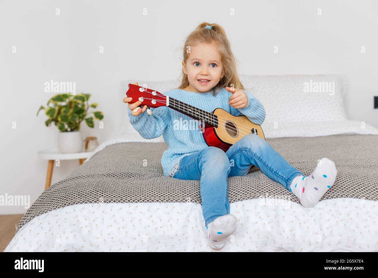 Carina bambina che gioca ukulele e lo canta a casa. 3 anni bambino imparare chitarra. Concetto di educazione della prima infanzia, hobby della musica, talento, h Foto Stock