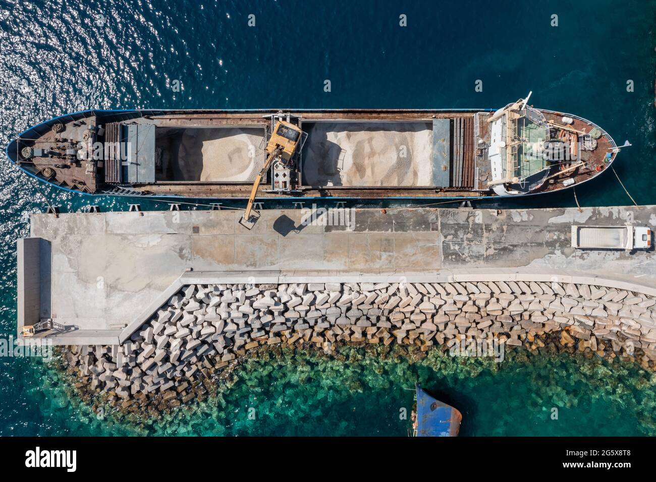 Attrezzature e macchinari per la costruzione di opere marine, drone aereo vista dall'alto, macchina per il carico di sabbia su una nave al porto di Korissia, isola di Kea Tzia, Cycla Foto Stock