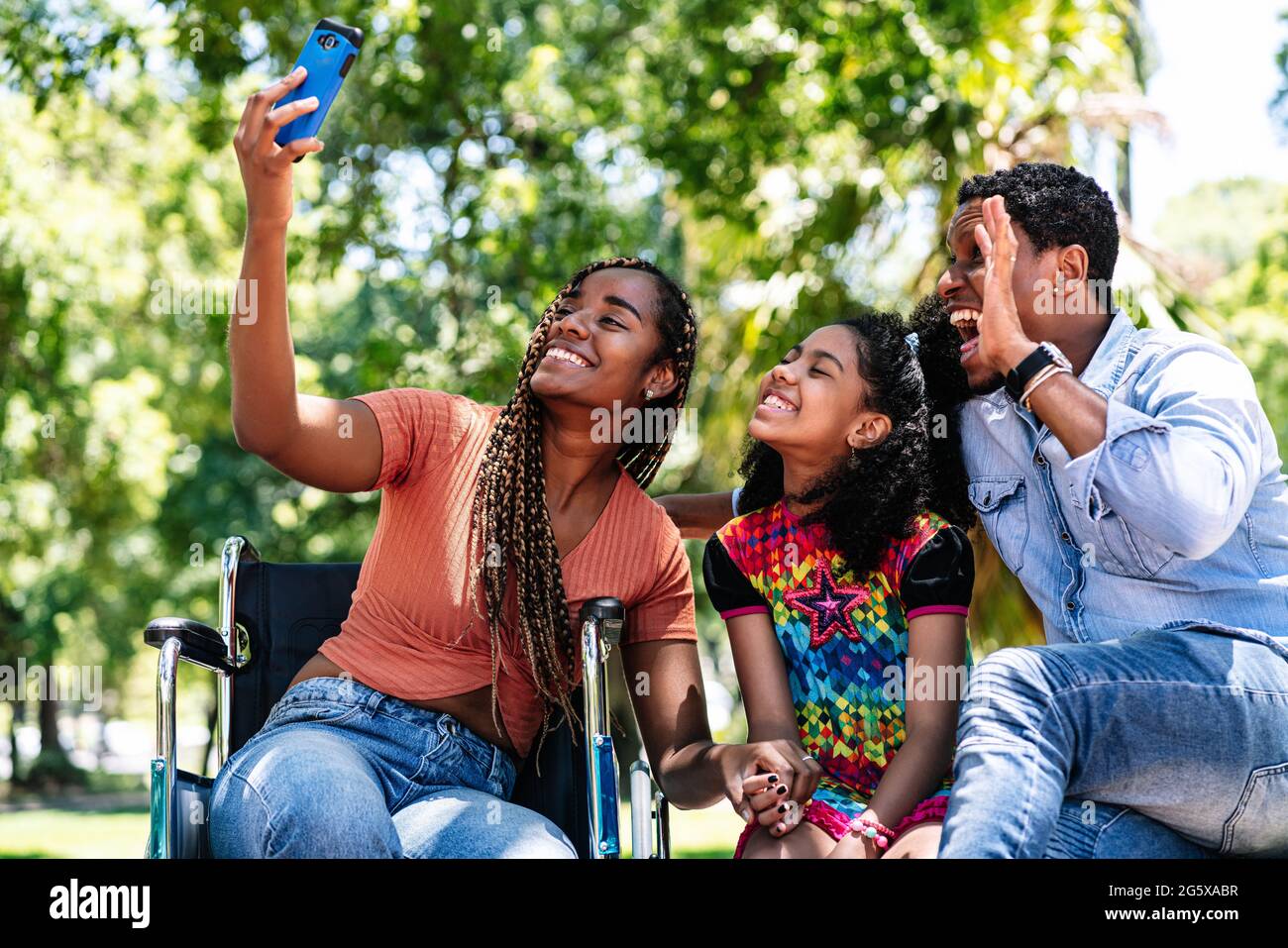 Donna in sedia a rotelle che prende un selfie con la sua famiglia. Foto Stock