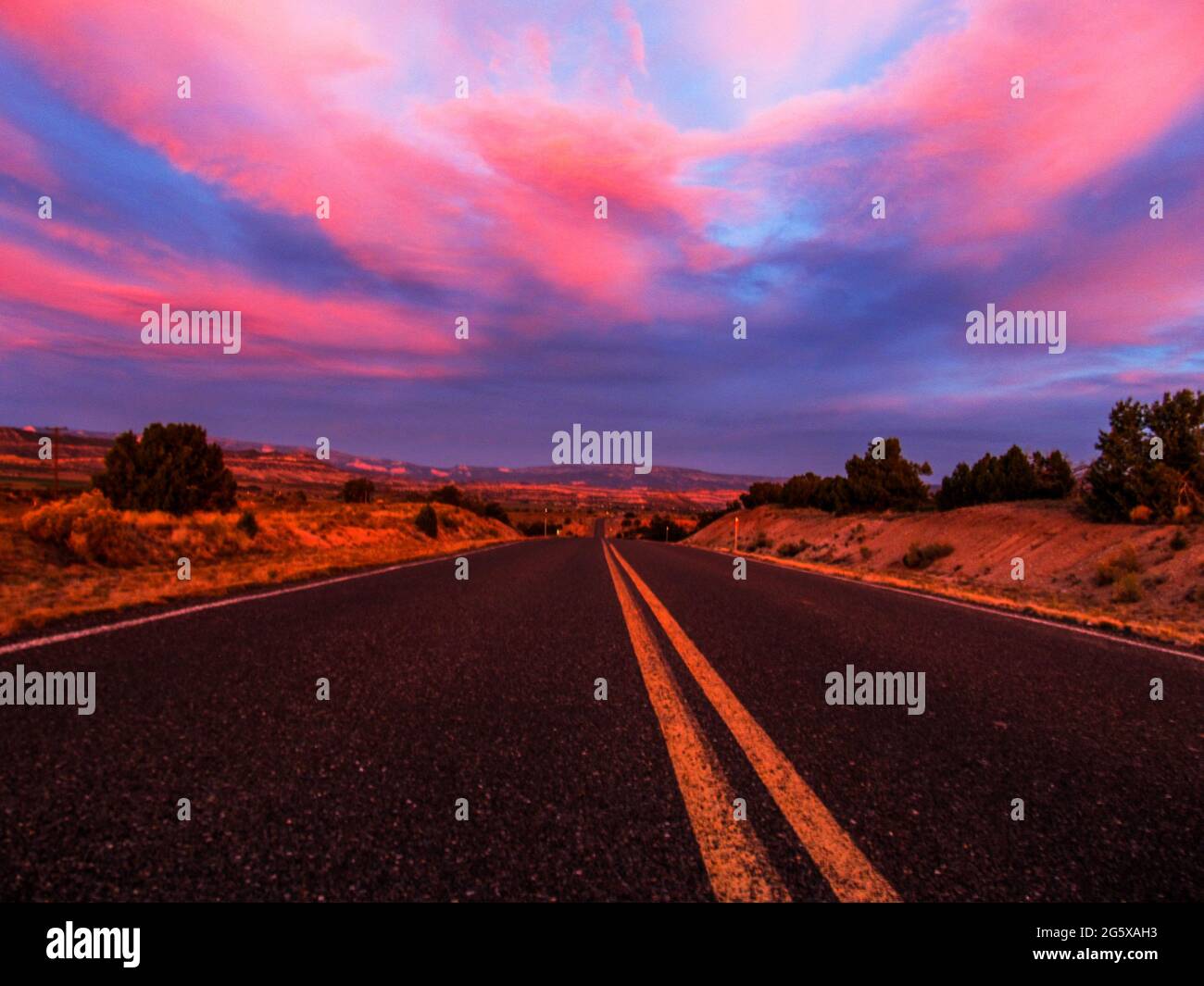 Guardando lungo l'autostrada 12, appena fuori Escalante, Utah, USA, alla prima luce del mattino, il sole che si alza colorando il cielo nelle sfumature di rosa e blu Foto Stock