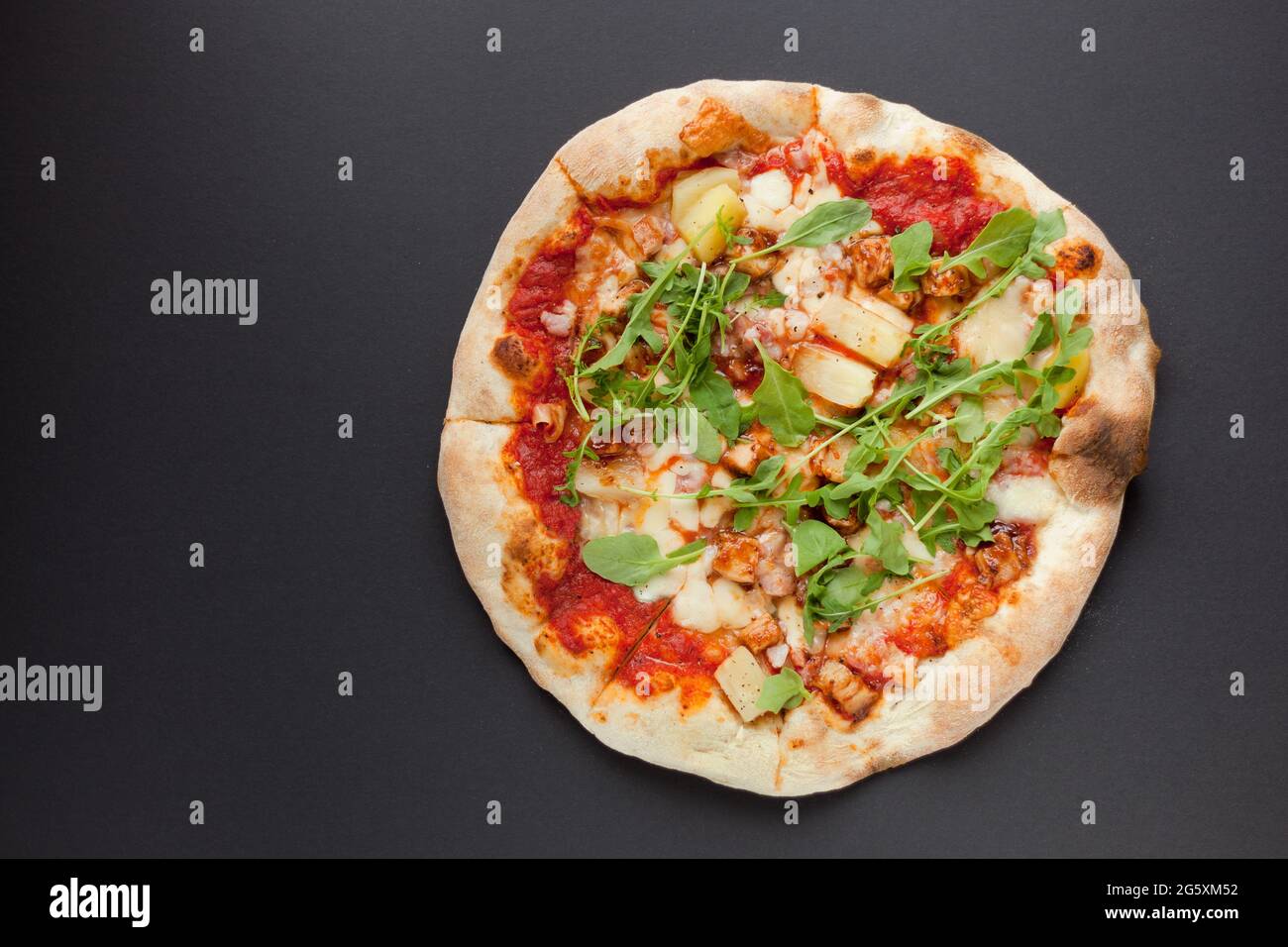 Pizza con prosciutto affumicato e rucola su fondo nero. Vista dall'alto. Gustosa pizza con carne su terreno scuro Foto Stock