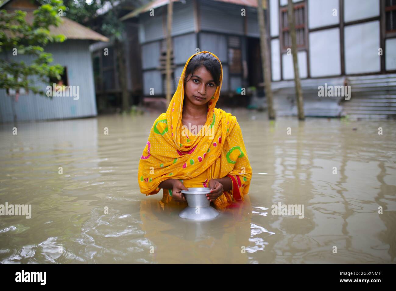 Una donna trasporta il vaso d'acqua mentre cammina attraverso l'acqua alluvionale durante l'alluvione monsonica a Munshiganj, vicino a Dhaka, Bangladesh il 28 luglio 2020. Oltre 9.6 milioni di persone sono state colpite da inondazioni monsoniche, devastando vaste aree dell’India, del Bangladesh e del Nepal. Foto Stock